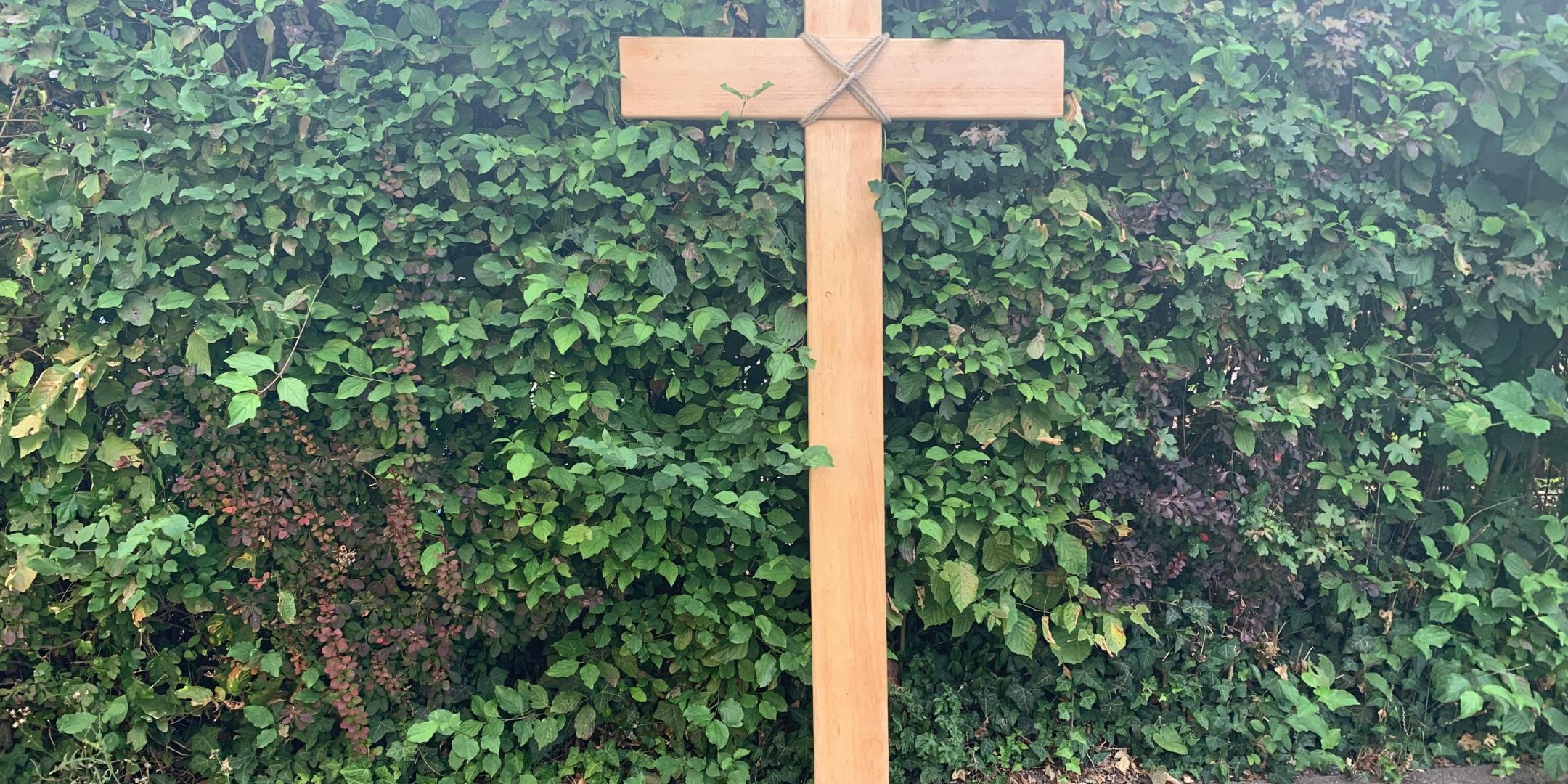 Weltjugendtagskreuz, auf Steinboden, vor einer Buchenhecke
