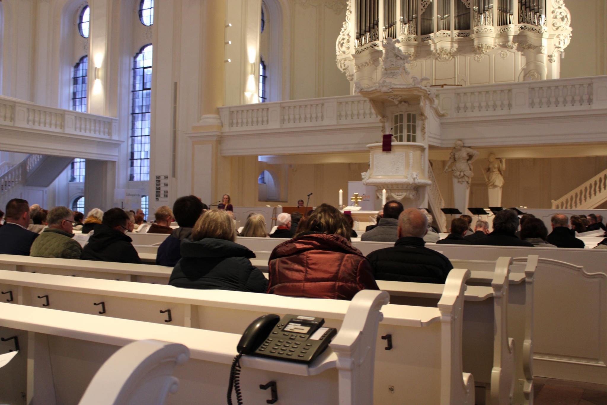 Menschen sitzen in den Kirchenbänken, auf den Bänken stehen Telefone
