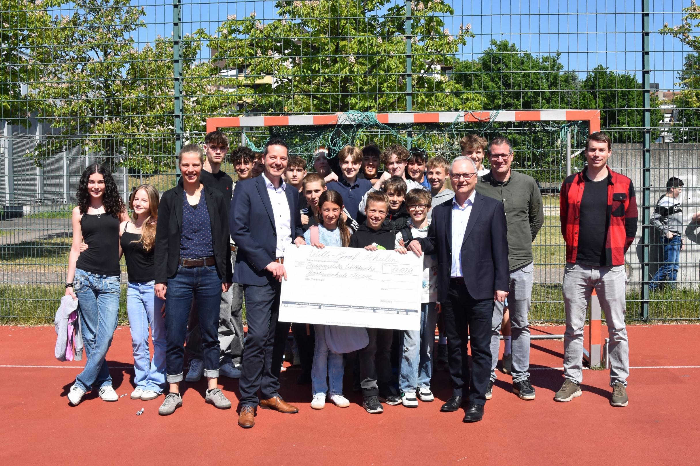 Schülerinnen und Schüler der Willi-Graf-Schulen und ihre Schulleiter Stefan Kilz und Stephan Arnold überreichen einen Scheck über 13.000 Euro an Thorsten Hoffmann und Katharina Nilles von der Diözesanstelle Weltkirche.
