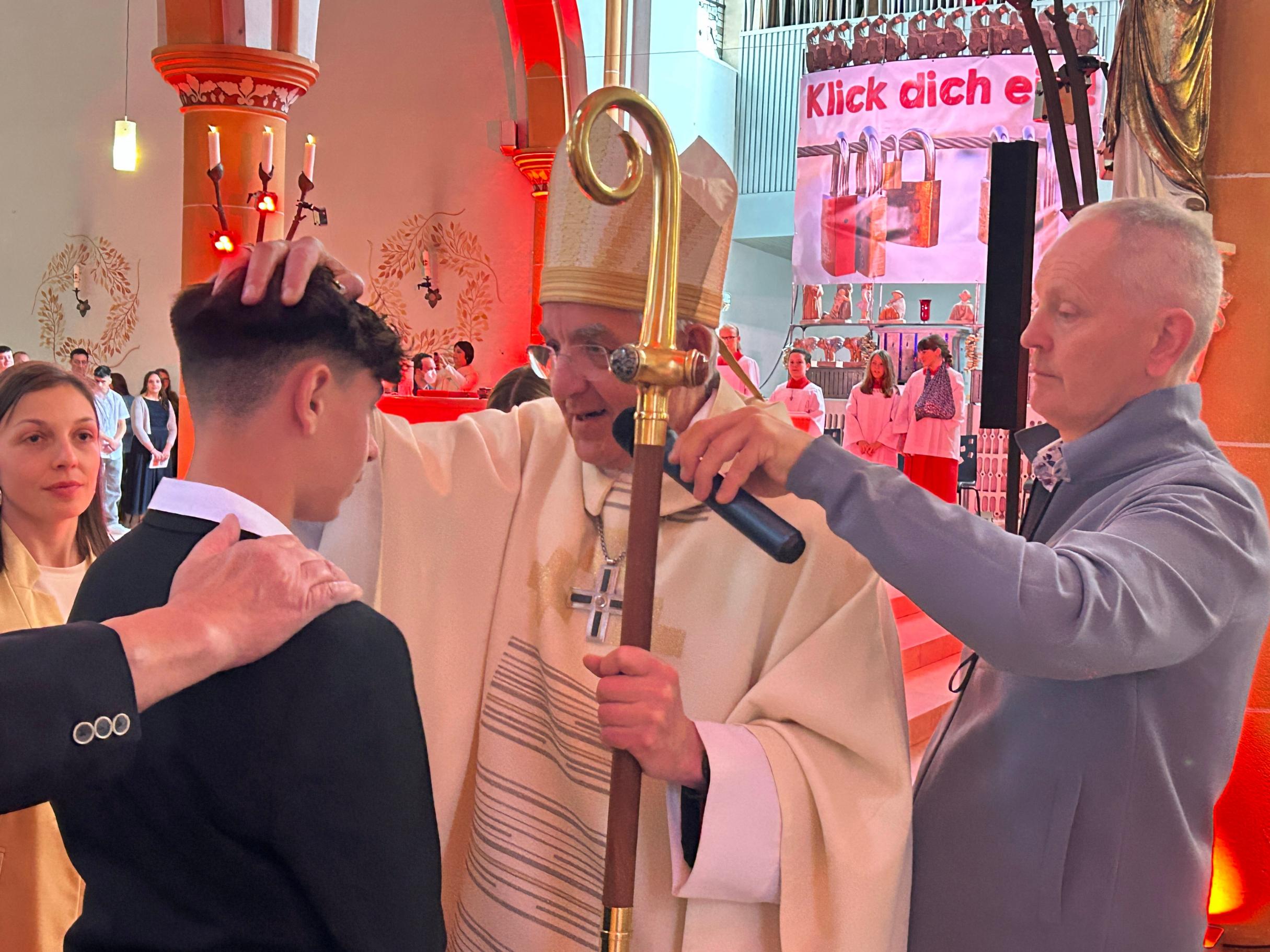 Ein Weihbischof mit Bischofsstab legt einem jungen Mann die Hand zur Firmung auf