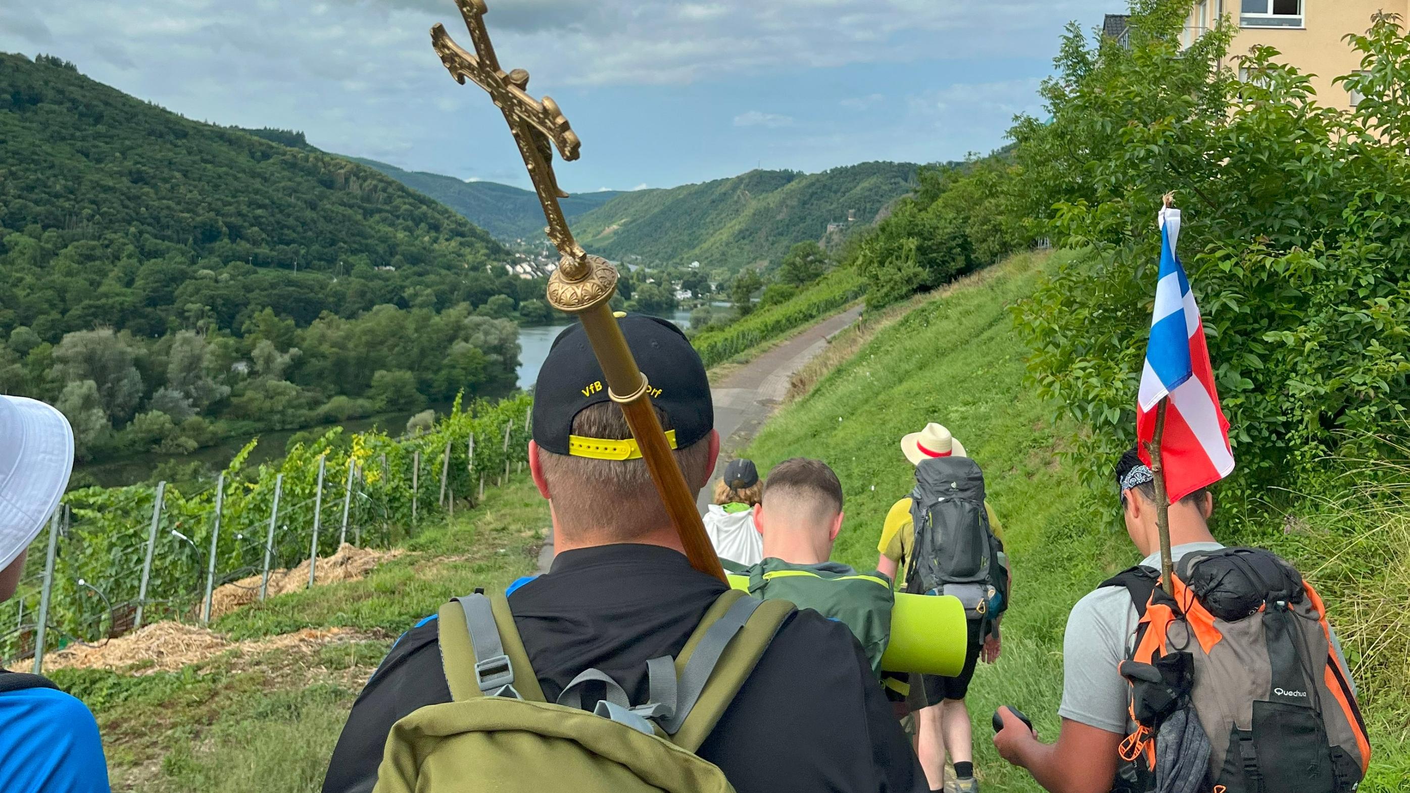 Eine Gruppe junger Menschen pilgert durch Weinberge