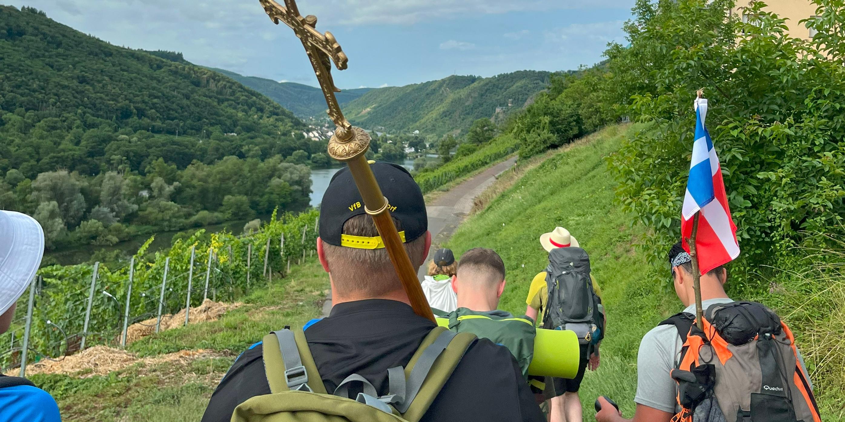 Eine Gruppe junger Menschen pilgert durch Weinberge
