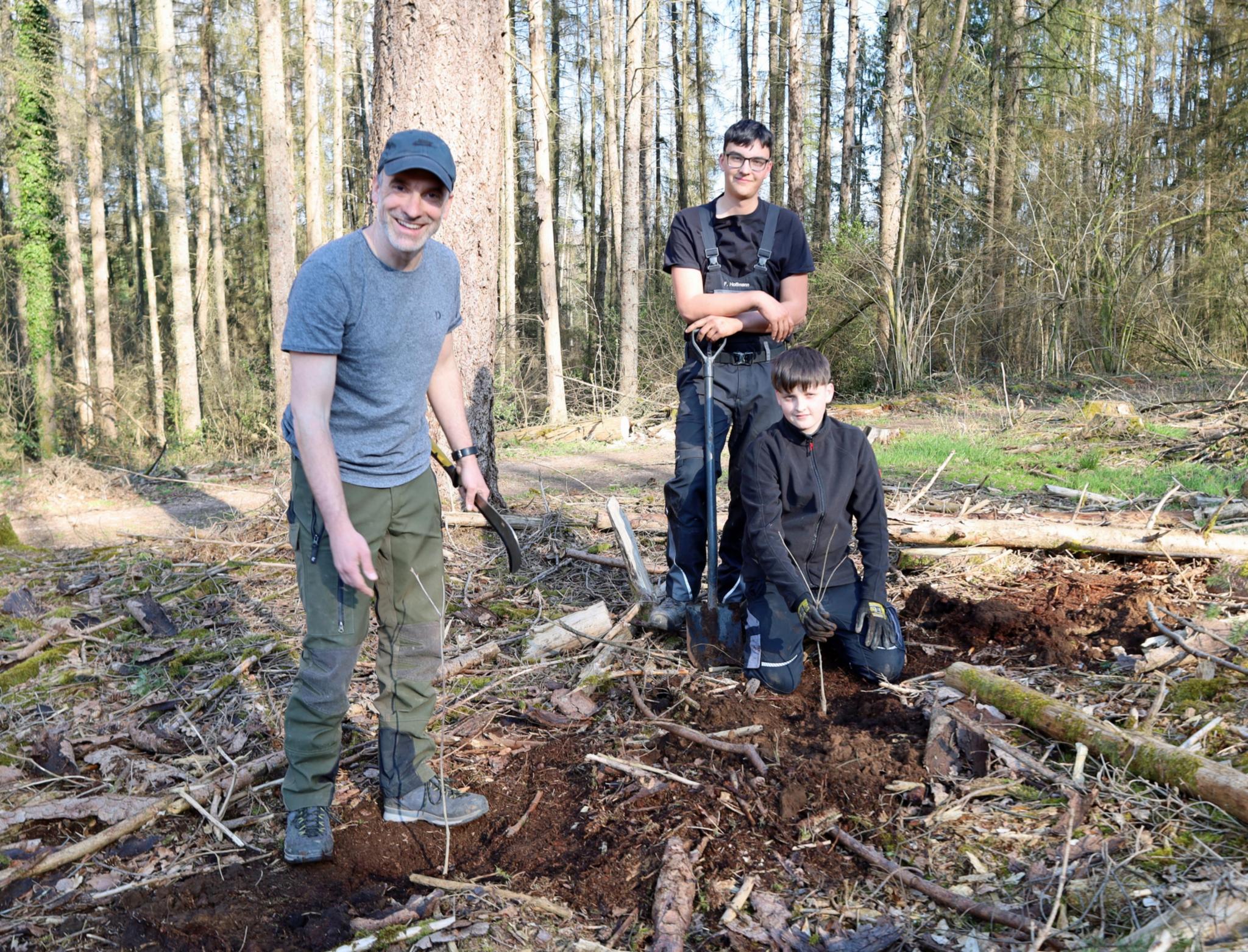 Eiche, Roteiche, Weißtanne und türkische Baumhasel – diese vier Baumarten hat Fortfachwirt Linnebach über eine Baumschule in Bad Ems für die Pflanzaktion besorgt. „Das sind alles trockenresistente Sorten, da es aufgrund des Klimawandels immer wärmer wird“, erklärt er der Gruppe. Dann wird es praktisch: „Macht vor dem Pflanzen auf jeden Fall den staubtrockenen Rohhumus weg und grabt mit dem Spaten bis zum braunen Mineralboden – sonst vertrocknen uns die Pflanzen“, gibt er genaue Anweisungen. Während sich die Jugendlichen an die Arbeit machen, geht er reihum und gibt Tipps: „Schau mal, der hier war nicht fest genug eingepflanzt“, sagt Linnebach und zieht einen Steckling ohne viel Kraft wieder raus. Jedes neue Bäumchen wird von den Firmberwerber*innen mit einem kleinen Stück Malerkrepp gekennzeichnet. „Das schützt vor Wildverbiss“, sagt Linnebach. Aus 50 Stecklingen wachsen ein bis zwei große Bäume. Aber auch die, die nicht groß werden, seien für das Ökosystem Wald wichtig, sagt der Experte: Sie spenden Schatten und sorgen somit für angenehmes Waldklima.  Aktuell bereiten sich rund 120 Jugendliche aus dem Pastoralen Raum Wadern auf ihre Firmung am 12. und 13. Juni vor. Dabei können sie aus zahlreichen Workshops das für sie passende Angebot wählen. Mit dabei sind Jakob aus Morscholz, Fabian aus Niederlosheim und Philipp aus Losheim. „Ich bin gerne draußen in der Natur“, sagt Jakob aus Morscholz und Fabian aus Niederlosheim ergänzt: „Ich packe gerne irgendwo mit an.“ Ein Stück weiter oben am Hang arbeiten Sasori, Shari und Nina. „Mein Papa arbeitet beim Forst, da kenne ich mich aus. Es ist wichtig, dass wir etwas tun, nachdem der Borkenkäfer vieles zerstört hat“, sagt Shari. „Wir haben viel über die Umwelt und den Klimawandel gesprochen, deswegen mache ich mit“, sagt Nina.  Finanziert wurden die jungen Bäume von Tierarzt Heiner Blasius, dem auch das Waldstück gehört, auf dem die Firmlinge die Stecklinge setzen. Zum Dank versorgte er die Jugendlichen während der Aktion mit Getränken und lud sie nach getaner Arbeit zum Grillen ein.