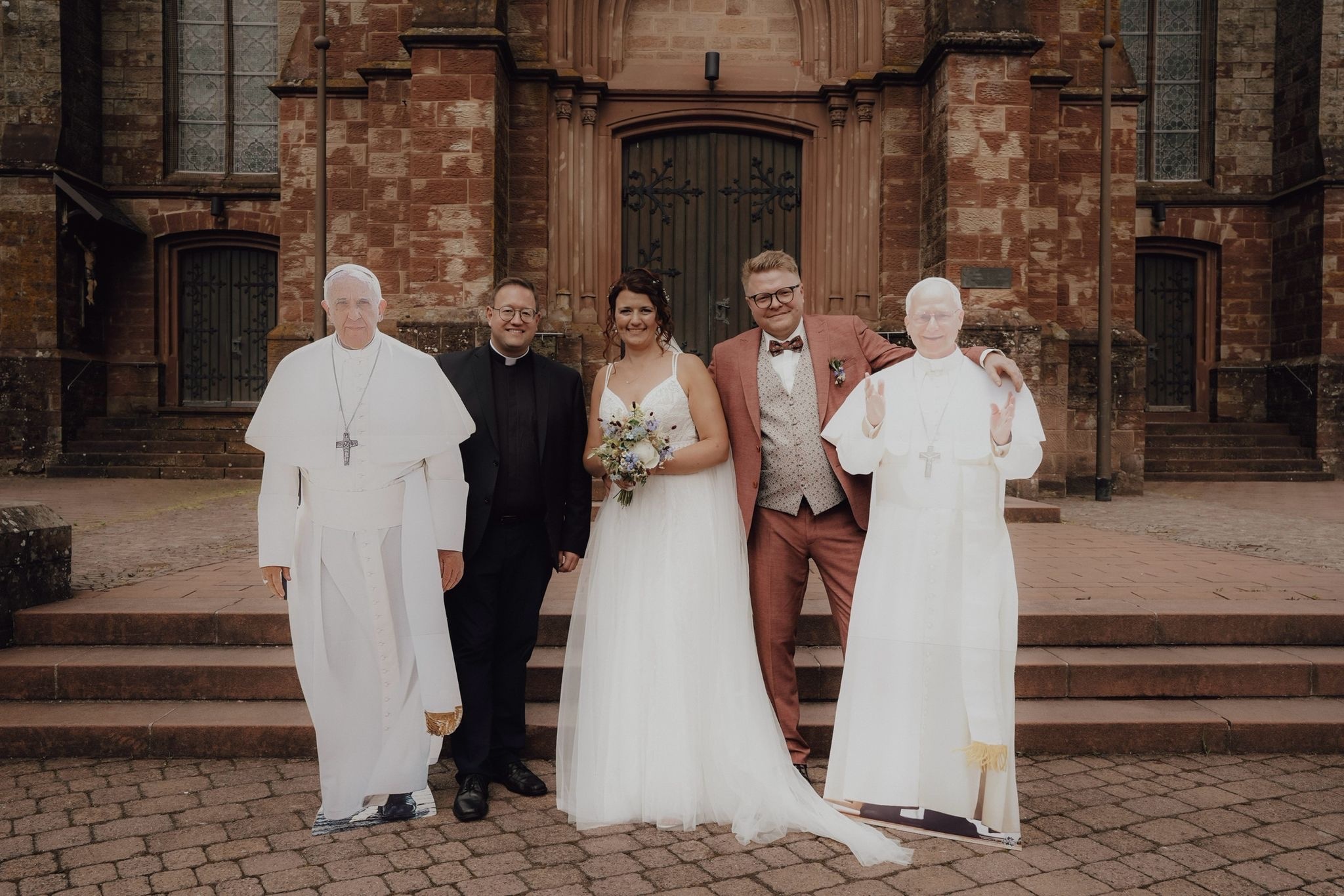 Hochzeit in Wadern-Nunkirchen: Das Brautpaar mit Pastor Jonas Weller und zwei Papstfiguren von Franziskus und Leo XIV.