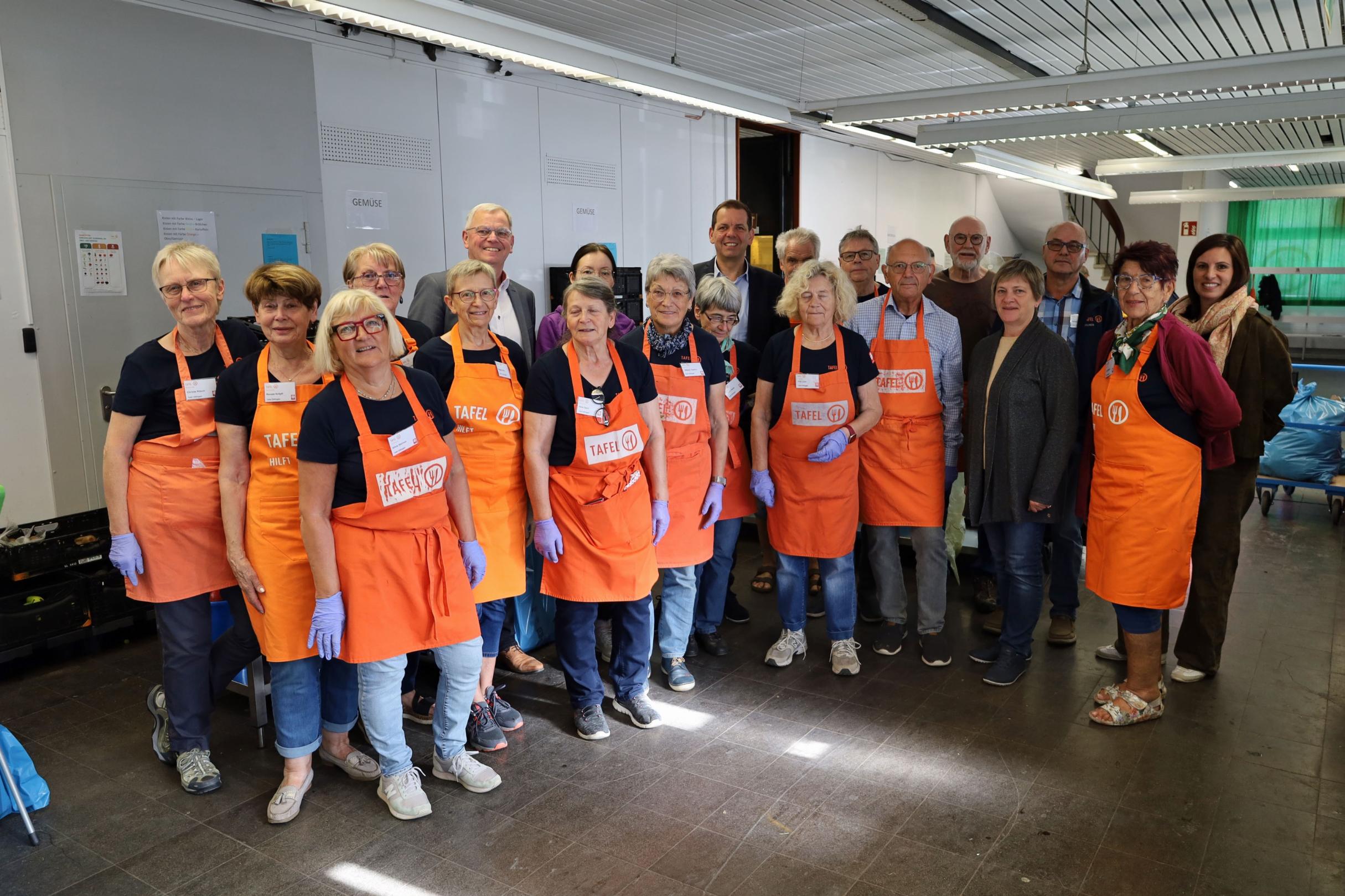 59 Ehrenamtliche helfen bei der Dillinger Tafel. Freitags bereiten sie die Lebensmittelausgabe vor. Gruppenfoto der Helfenden der Dillinger Tafel; die Personen haben alle Schürzen an