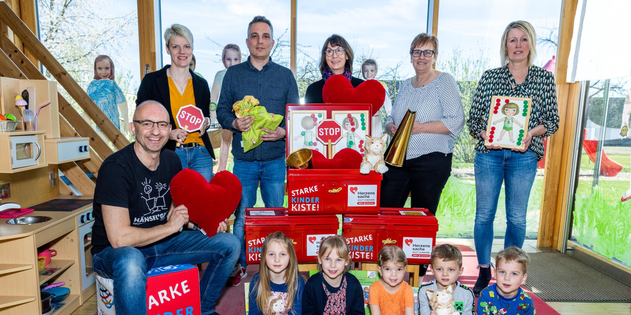 Kinder und Erwachsene mit Mini-STOP-Schildern, Spielsachen und einer Puppenküche