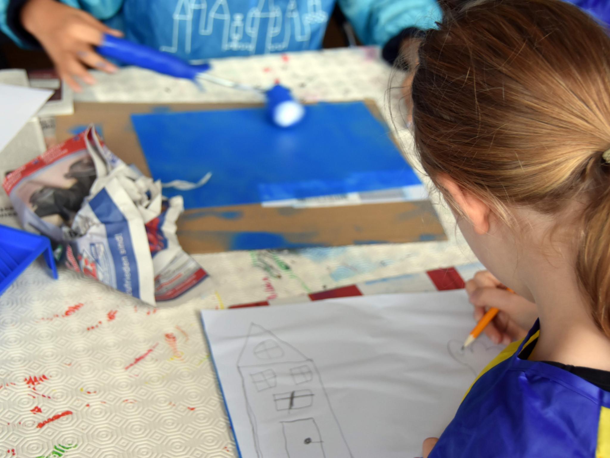 Mit einer Farbrolle wird blaue Farbe auf eine Glasplatte aufgetragen, darauf ein Papier gelegt und schon kann es losgehen.