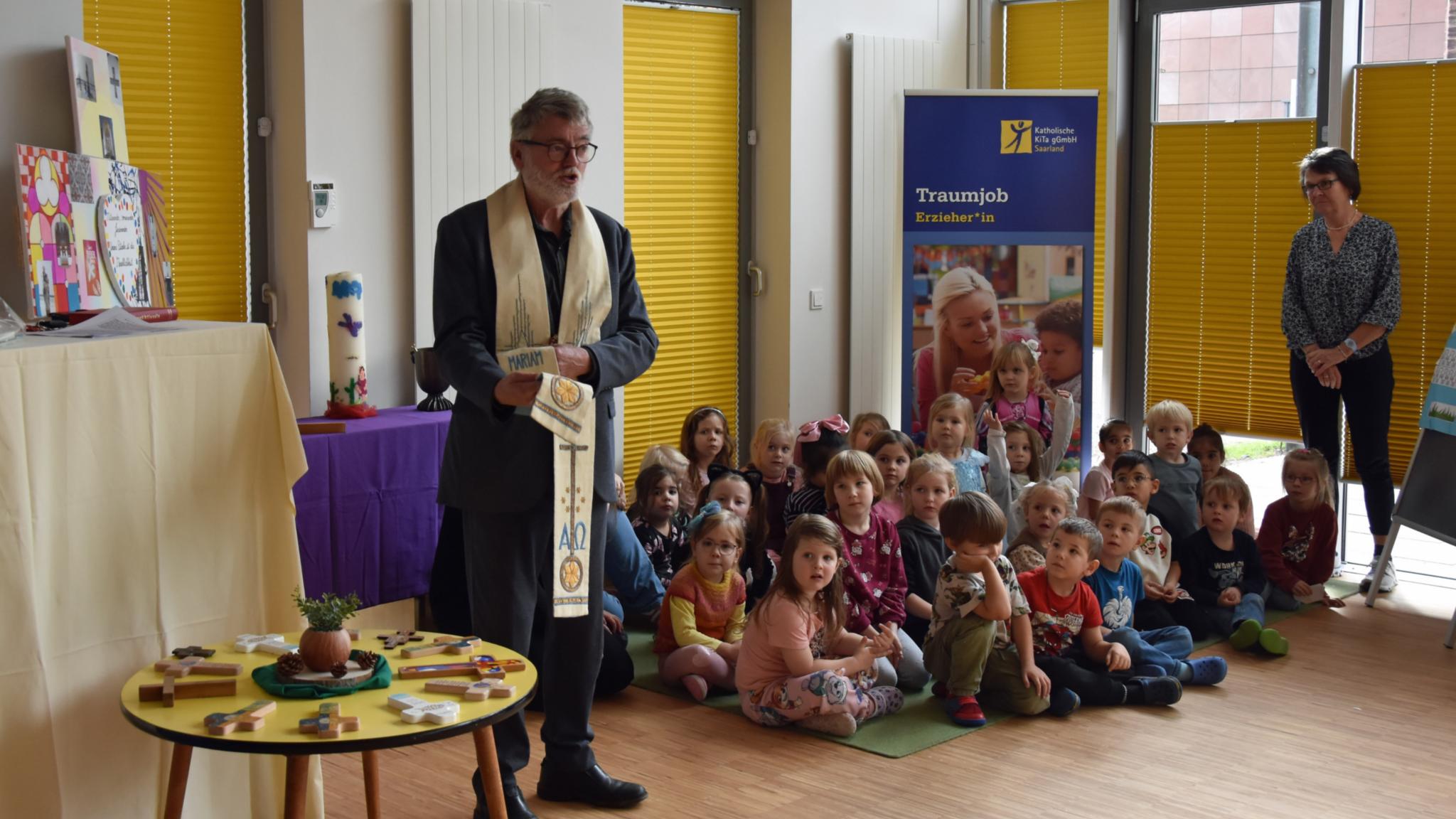Eine Gruppe Kinder sitzt auf dem Boden, daneben steht ein Pfarrer