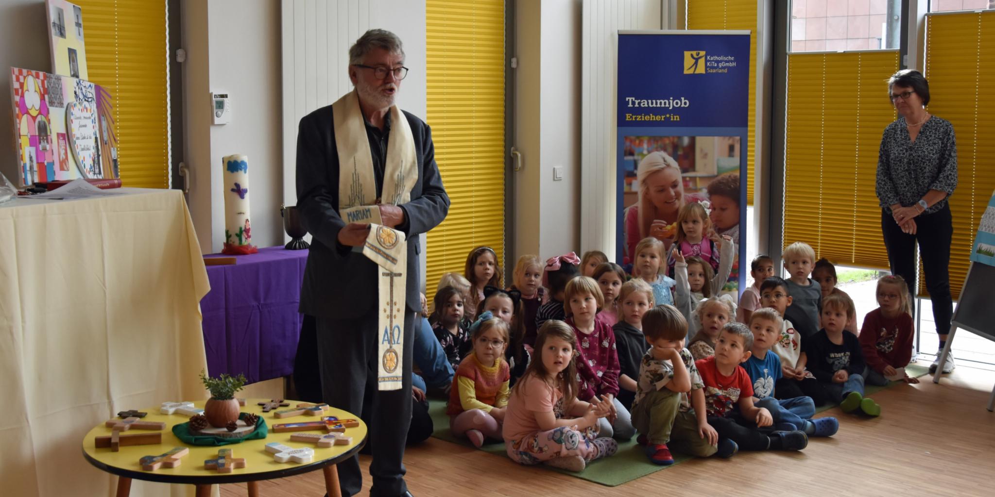 Eine Gruppe Kinder sitzt auf dem Boden, daneben steht ein Pfarrer