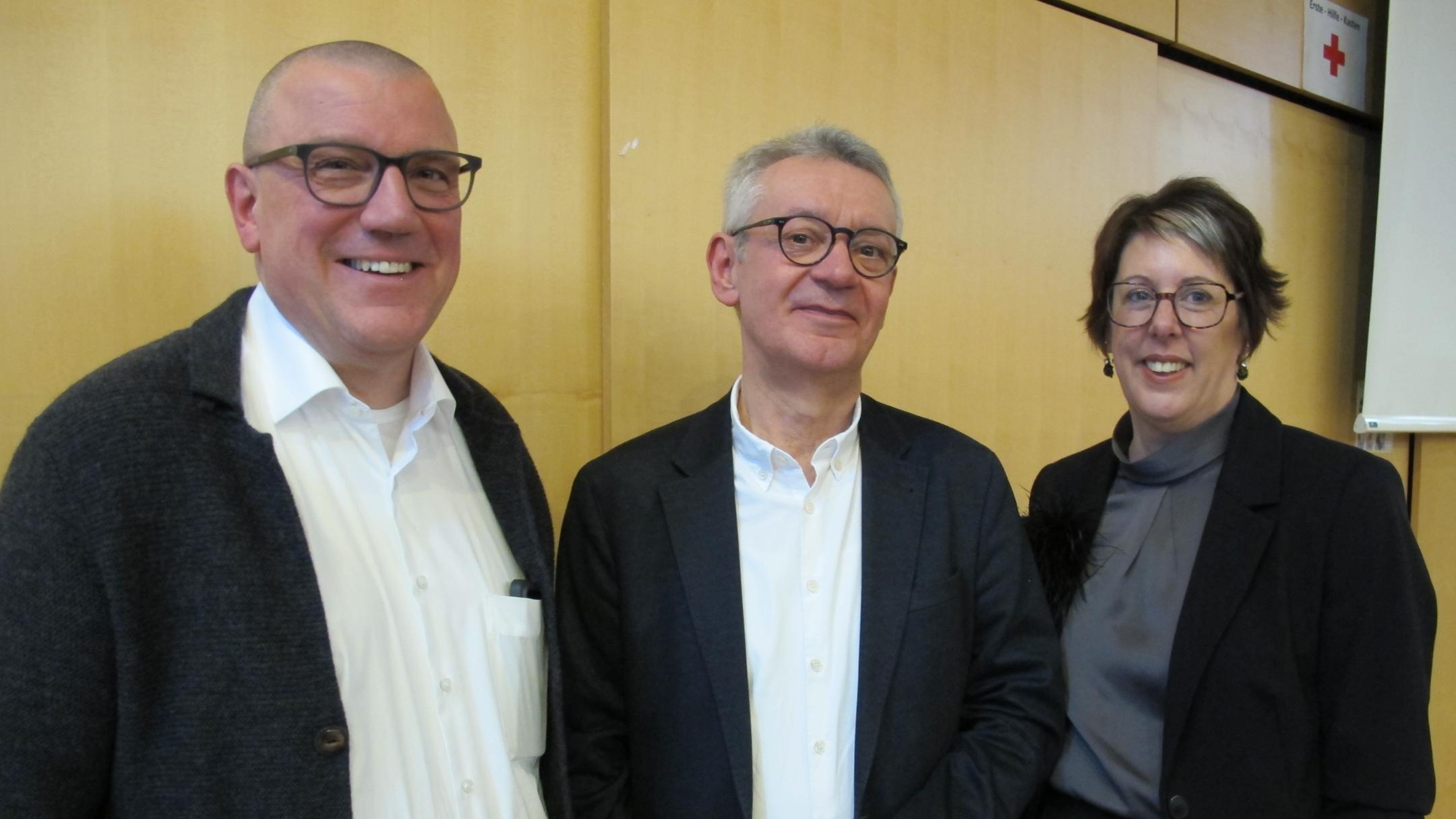 Zwei Männer und eine Frau stehen für ein Gruppenbild zusammen.