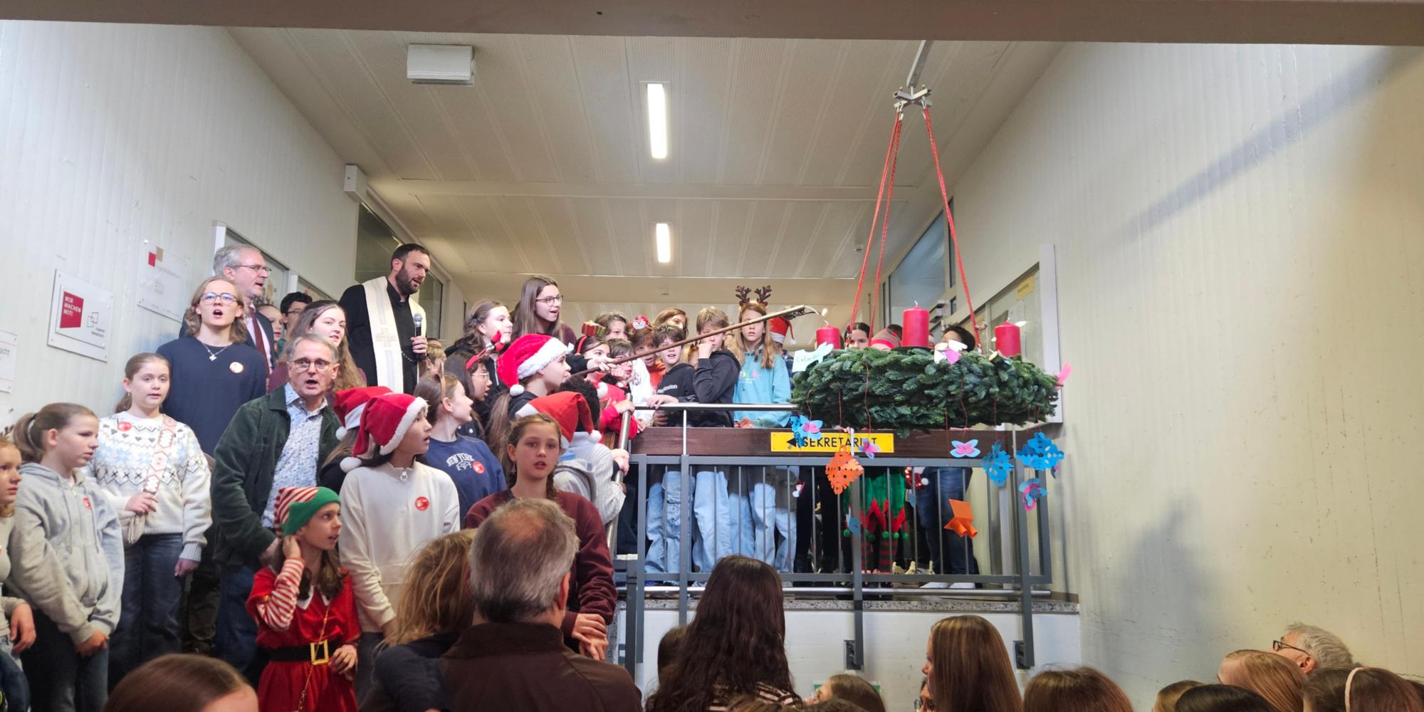 Schulpfarrer Dominic Lück segnet und entzündet gemeinsam mit der Schülervertretung die erste Kerze am Adventskranz.