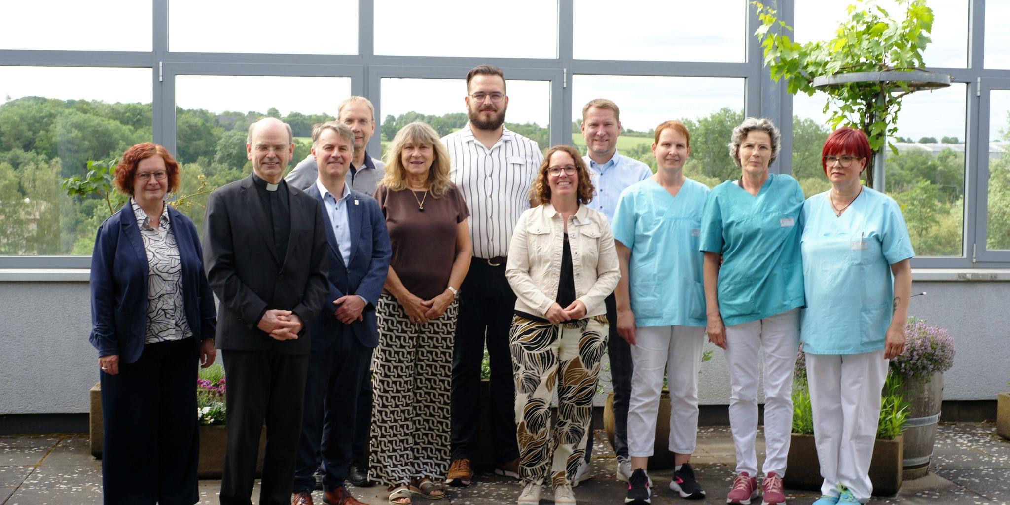 Ein Gruppenfoto, auf dem auch Menschen in hellblauer Pflegekleidung zu sehen sind.