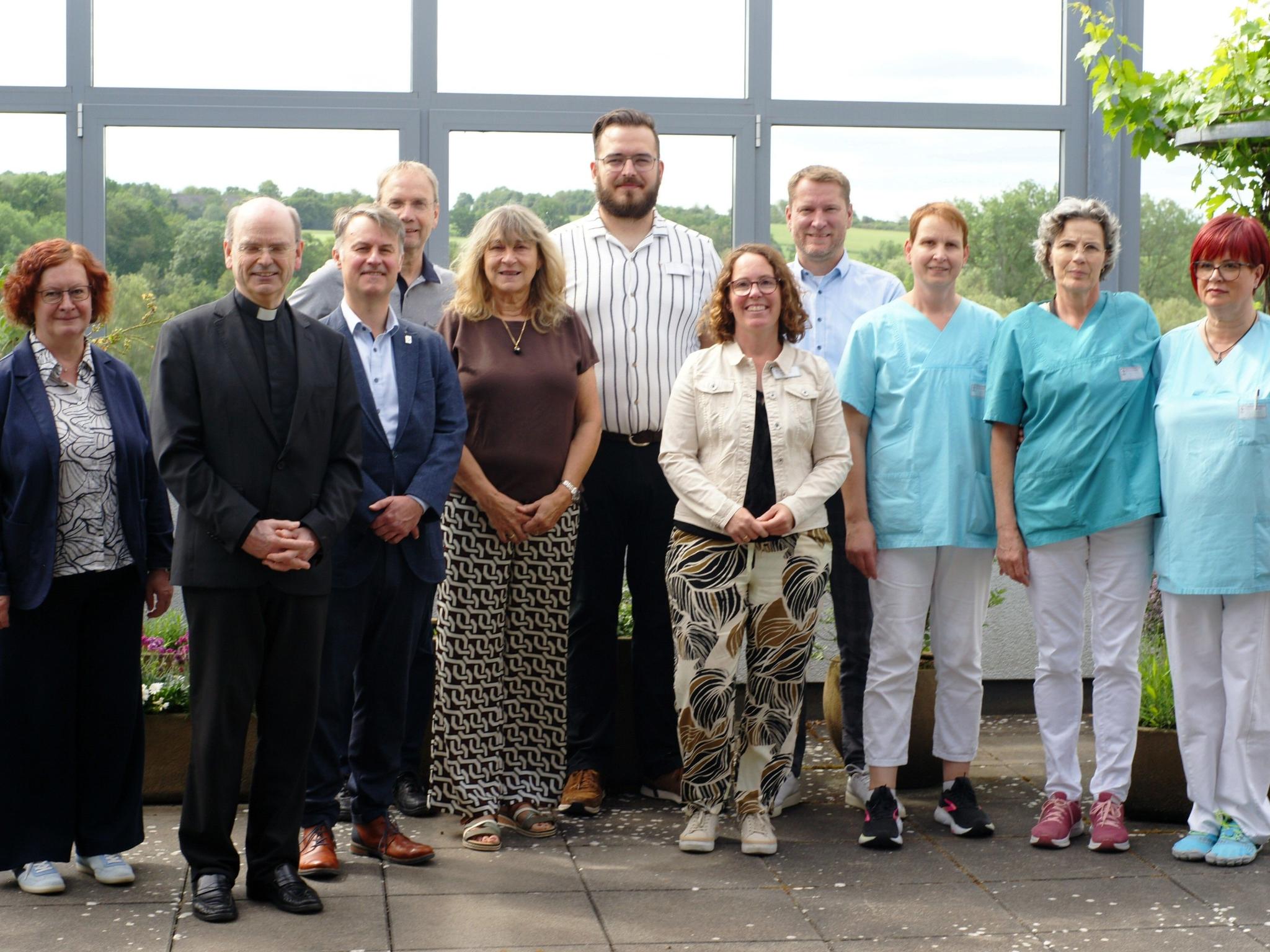 Ein Gruppenfoto, auf dem auch Menschen in hellblauer Pflegekleidung zu sehen sind.