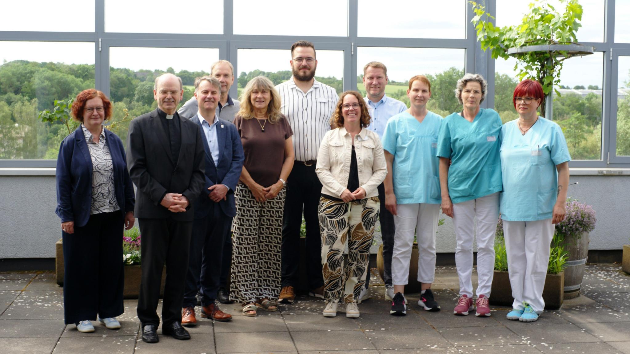 Ein Gruppenfoto, auf dem auch Menschen in hellblauer Pflegekleidung zu sehen sind.