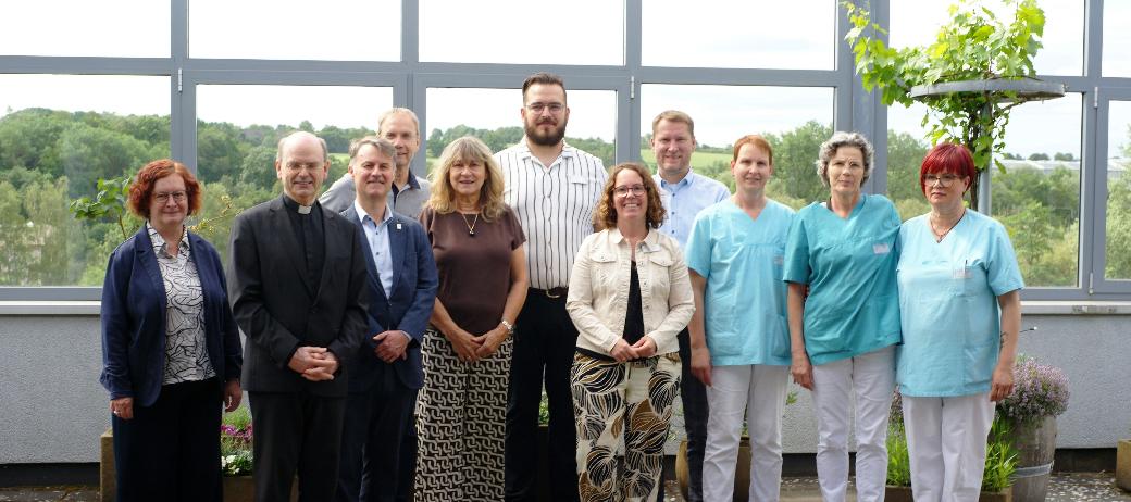 Ein Gruppenfoto, auf dem auch Menschen in hellblauer Pflegekleidung zu sehen sind.
