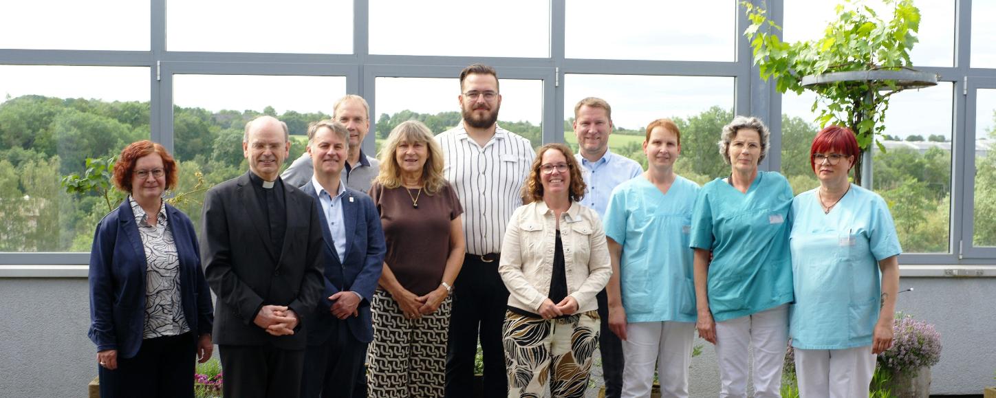 Ein Gruppenfoto, auf dem auch Menschen in hellblauer Pflegekleidung zu sehen sind.