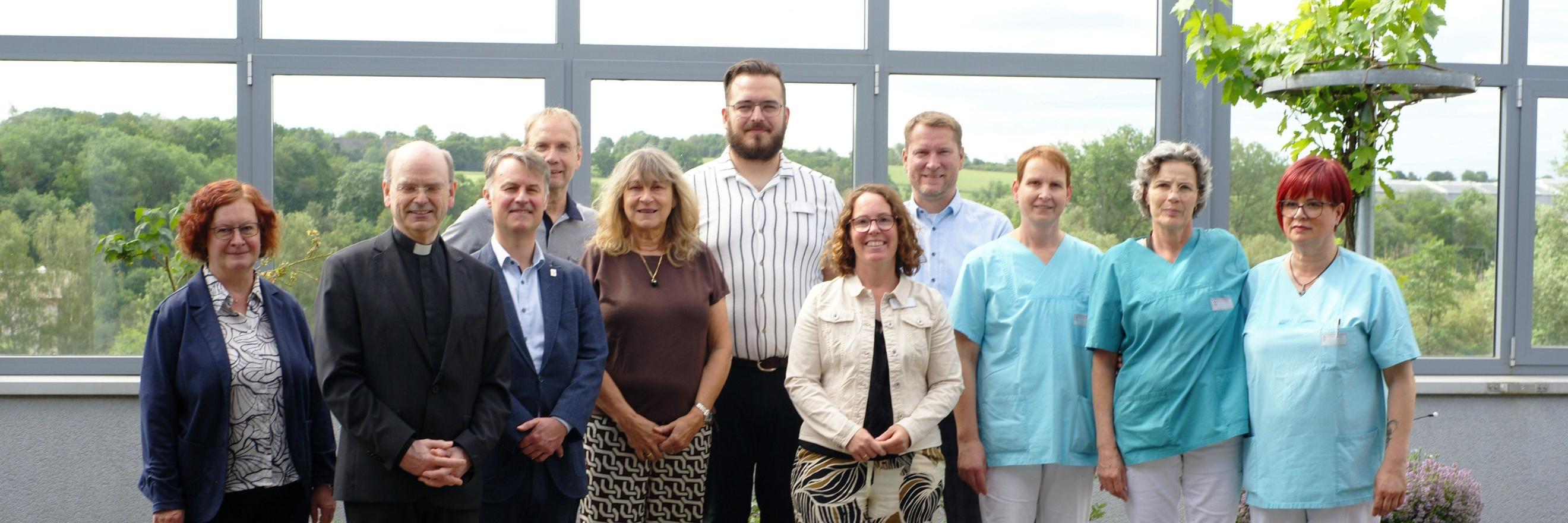 Ein Gruppenfoto, auf dem auch Menschen in hellblauer Pflegekleidung zu sehen sind.