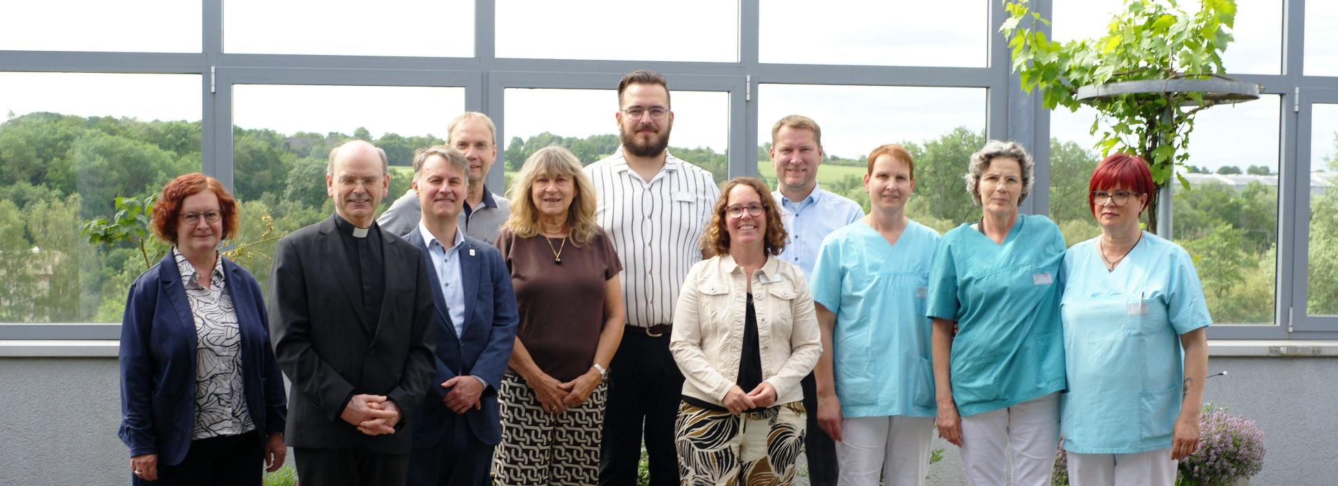 Ein Gruppenfoto, auf dem auch Menschen in hellblauer Pflegekleidung zu sehen sind.