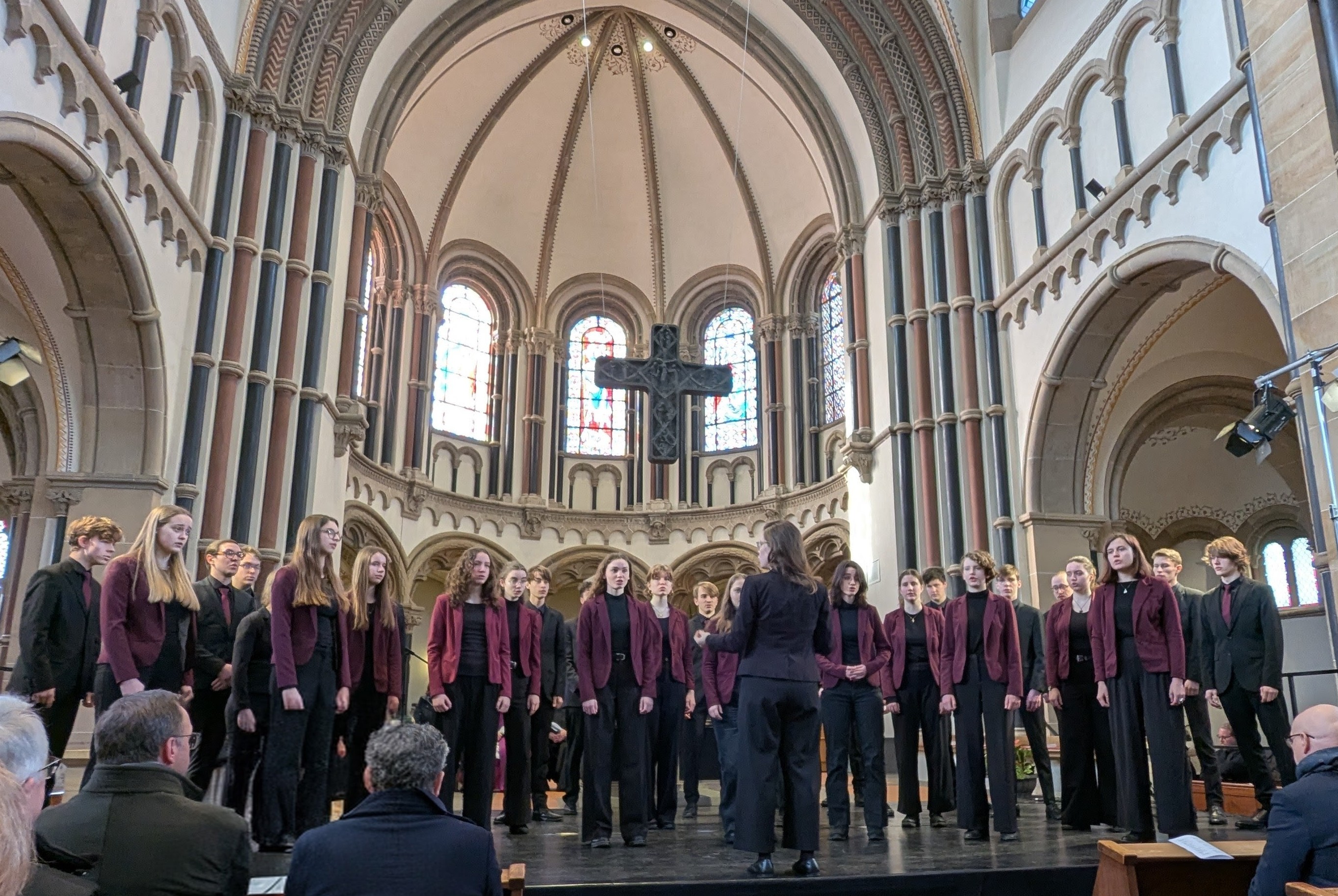 Eine große Gruppe junger Menschen steht auf einer Bühne vor einem Altar und singt.