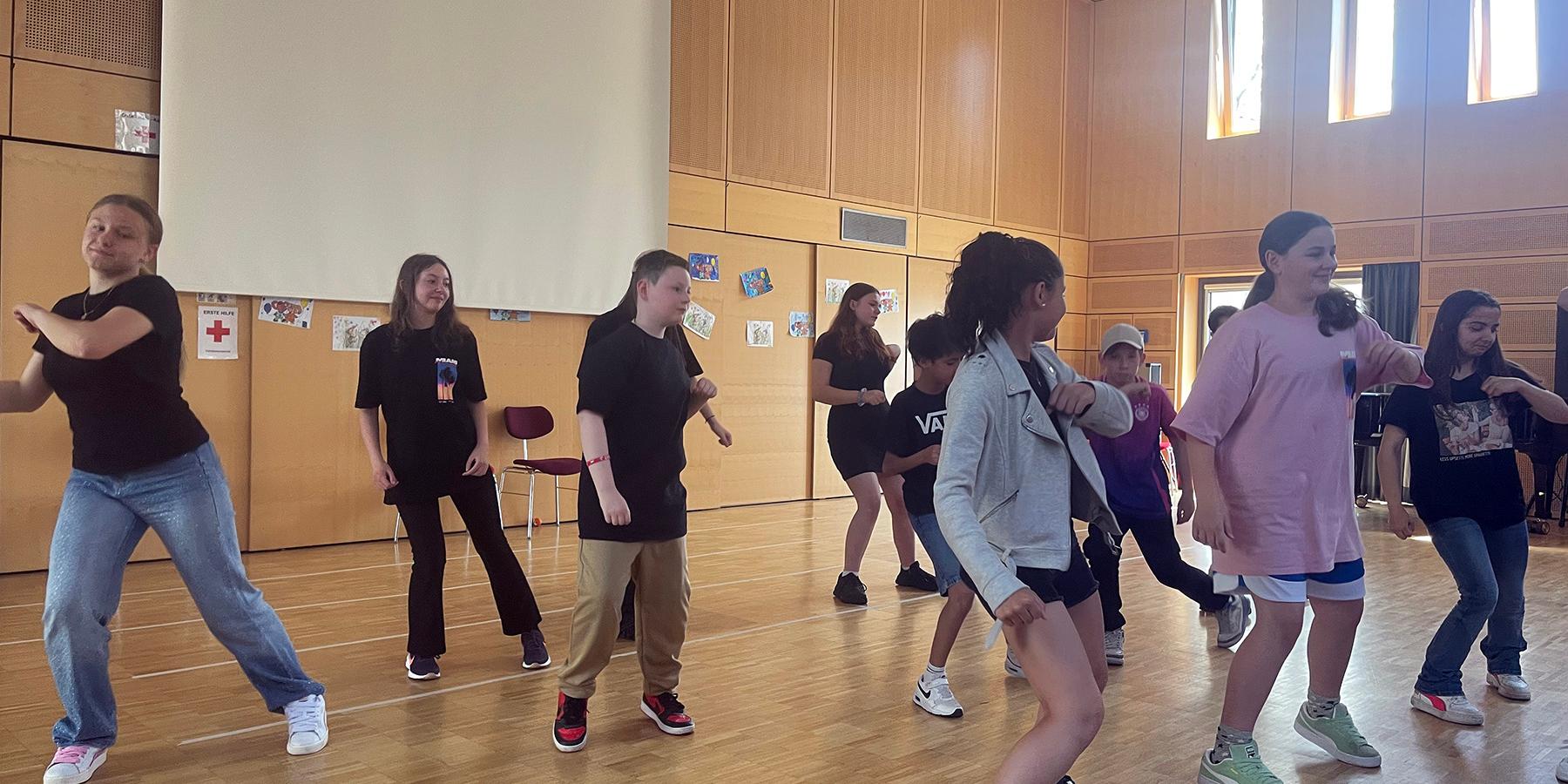 Eine Gruppe von Kindern tanzen im Rahmen einer Aufführung in einer Aula