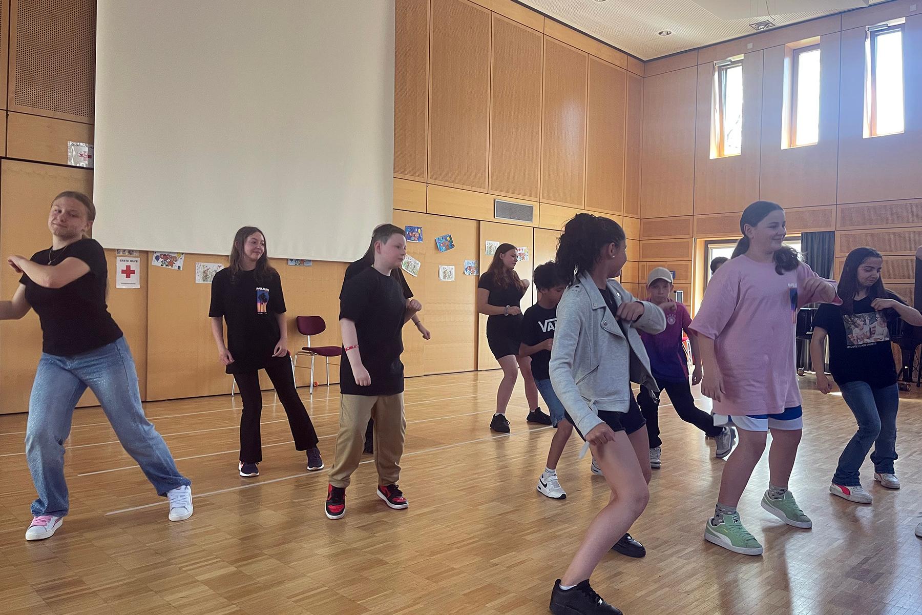 Eine Gruppe von Kindern tanzen im Rahmen einer Aufführung in einer Aula