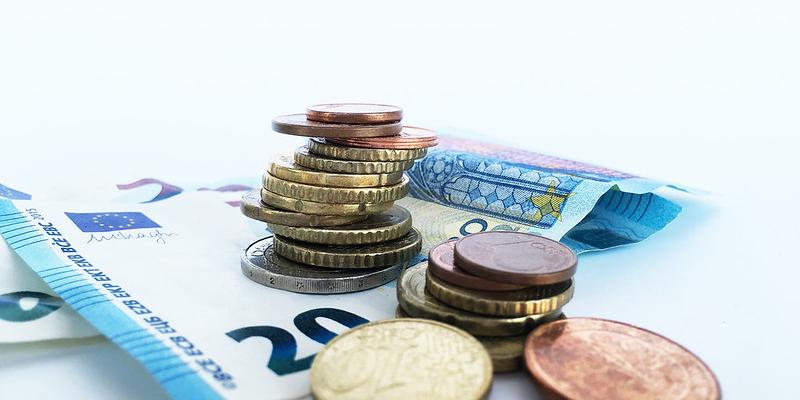 Das Foto zeigt in Großaufnahme vor weißem Hintergrund einen 20-Euro-Schein und darauf und daneben gestapelt Euro- und Cent-Münzen.