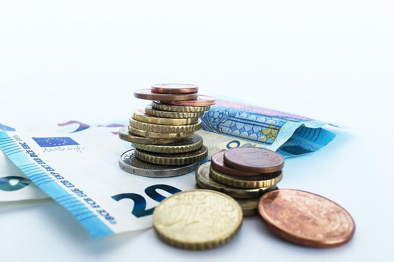 Das Foto zeigt in Großaufnahme vor weißem Hintergrund einen 20-Euro-Schein und darauf und daneben gestapelt Euro- und Cent-Münzen.