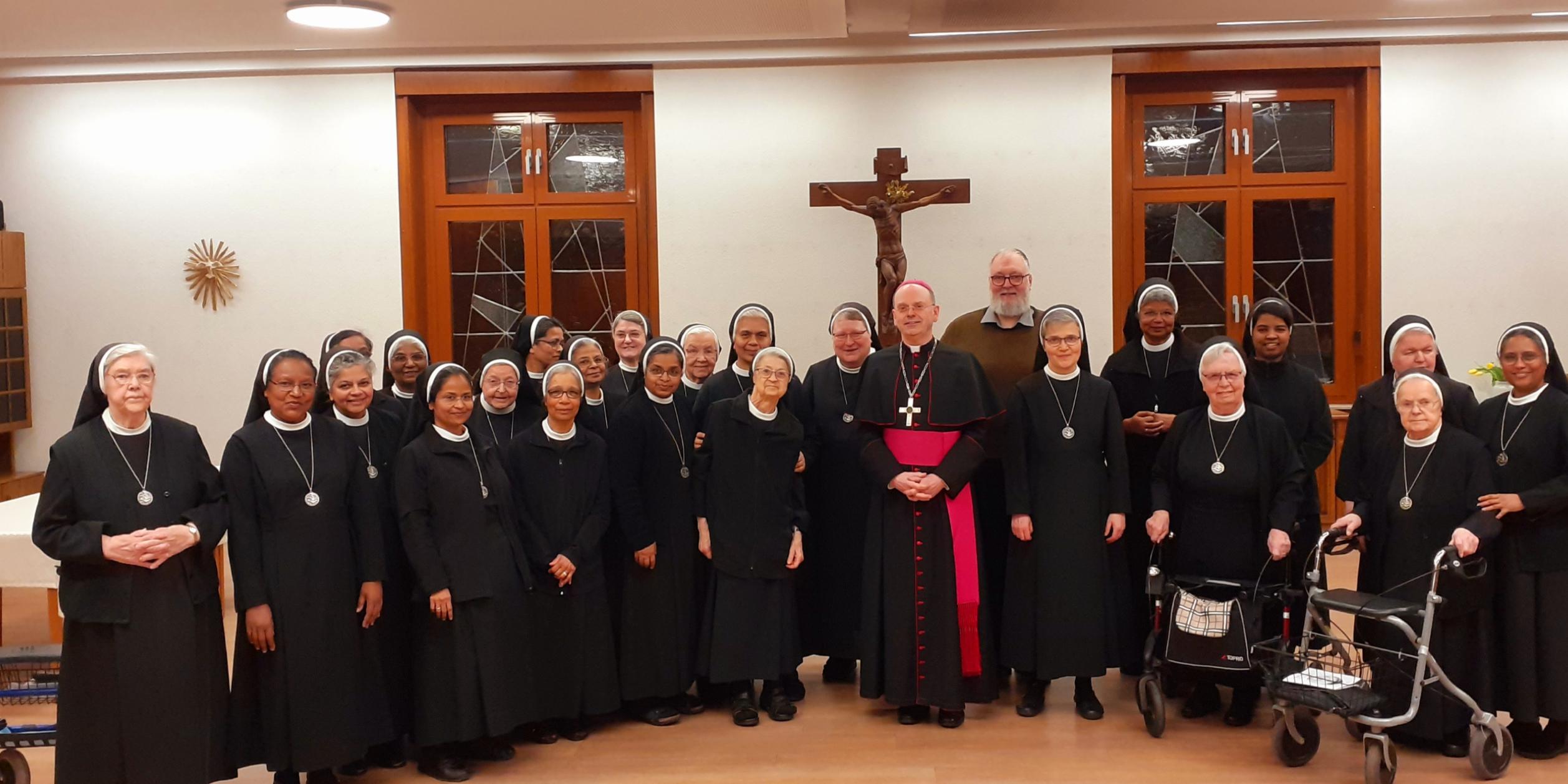Viele Ordensschwestern stehen um Weihbischof Brahm lächelnd für ein Gruppenfoto zusammen.