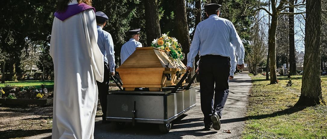 Ein Sarg wird auf einem Friedhof zum Grab getragen.