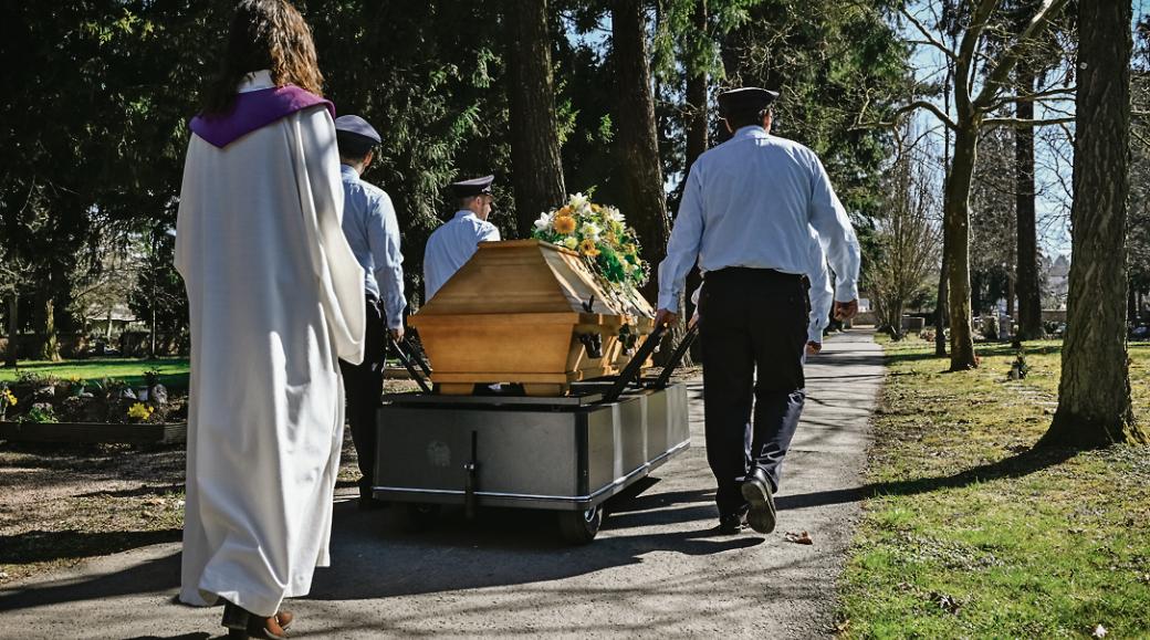 Ein Sarg wird auf einem Friedhof zum Grab getragen.