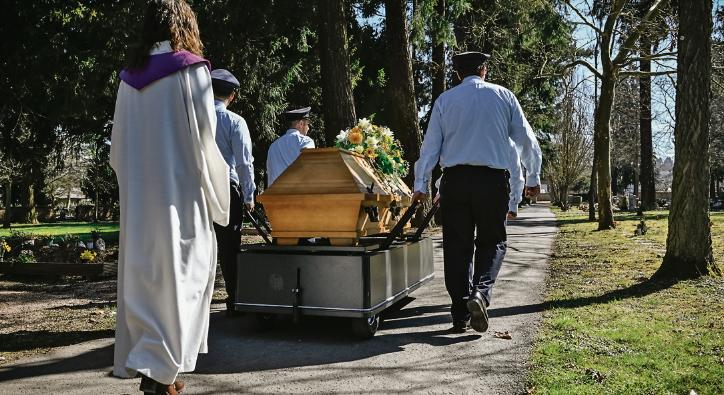 Ein Sarg wird auf einem Friedhof zum Grab getragen.