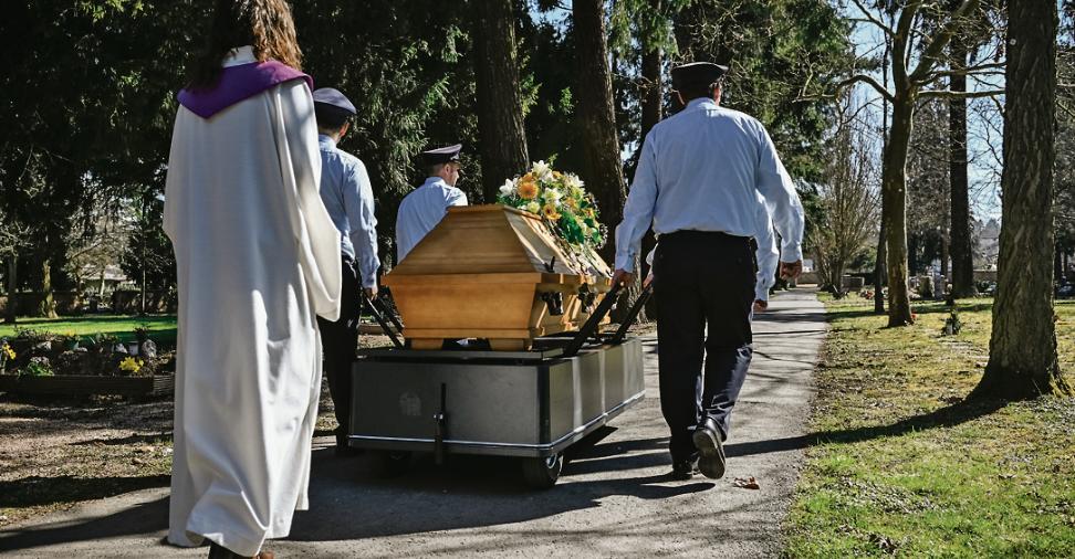 Ein Sarg wird auf einem Friedhof zum Grab getragen.