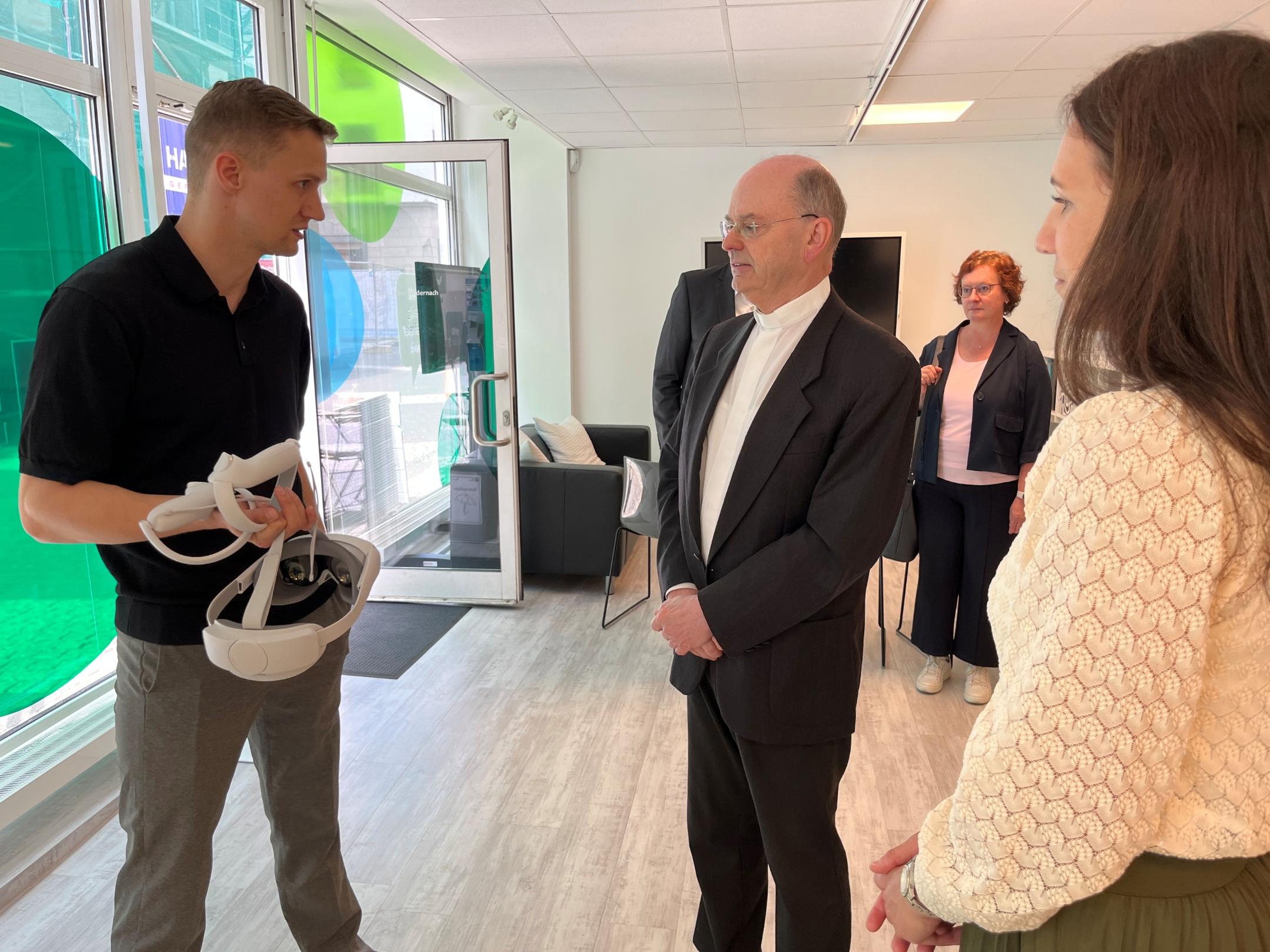 Der Leiter des PIKSL-Labors in Andernach, Jannik Junglas, (links) und die Mitarbeiterin Angela Nachtsheim erläutern Weihbischof Robert Brahm das Einsatzfeld einer Virtual-Reality-Brille.