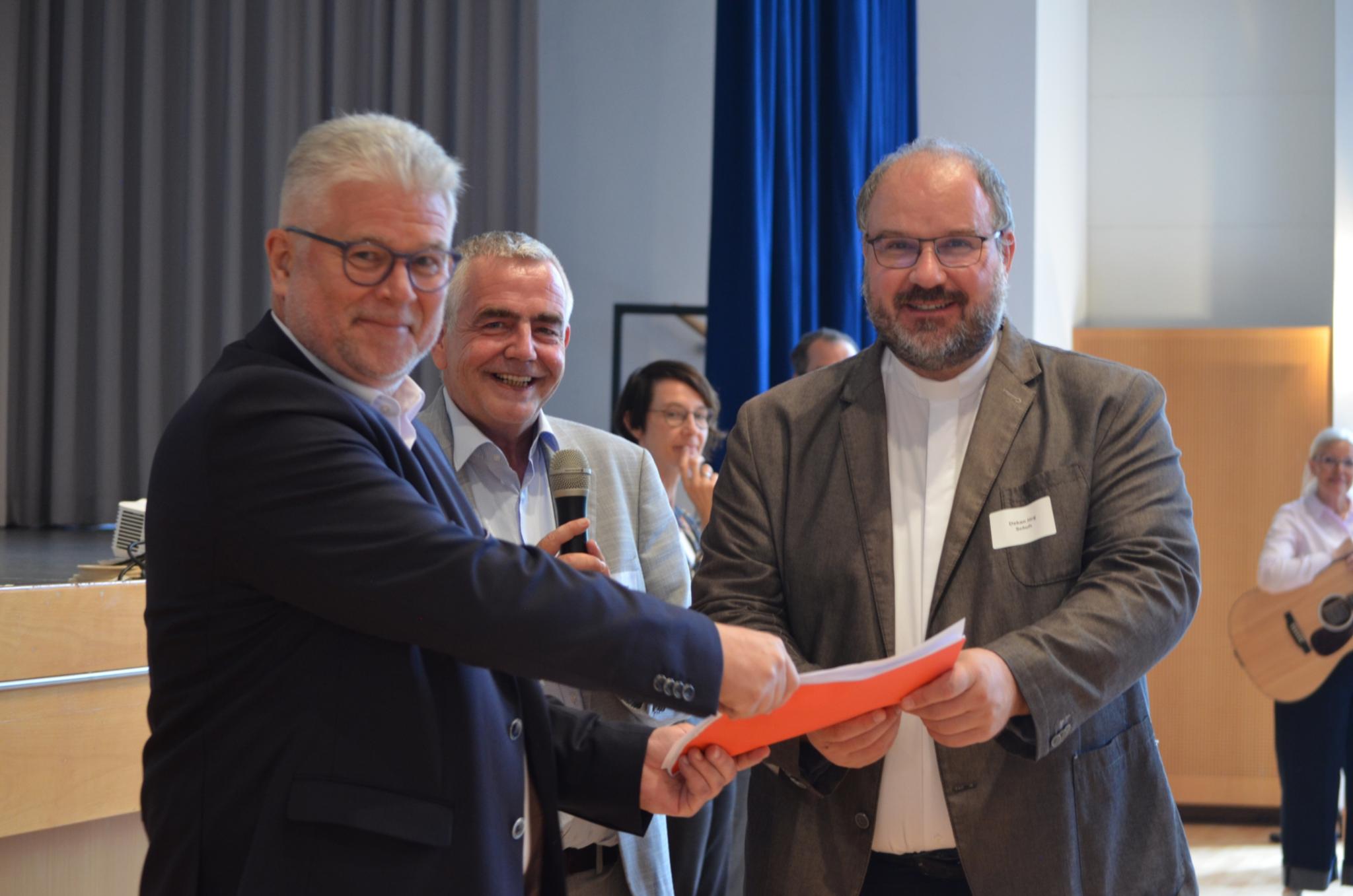 Die in Gesprächsrunden gesammelten Anliegen und Empfehlungen der Synodalversammlung wurden in einer roten Mappe an Dekan Jörg Schuh (rechts) und an den Vorsitzenden des Rates des Pastoralen Raumes Rainer Dinger (links) übergeben.