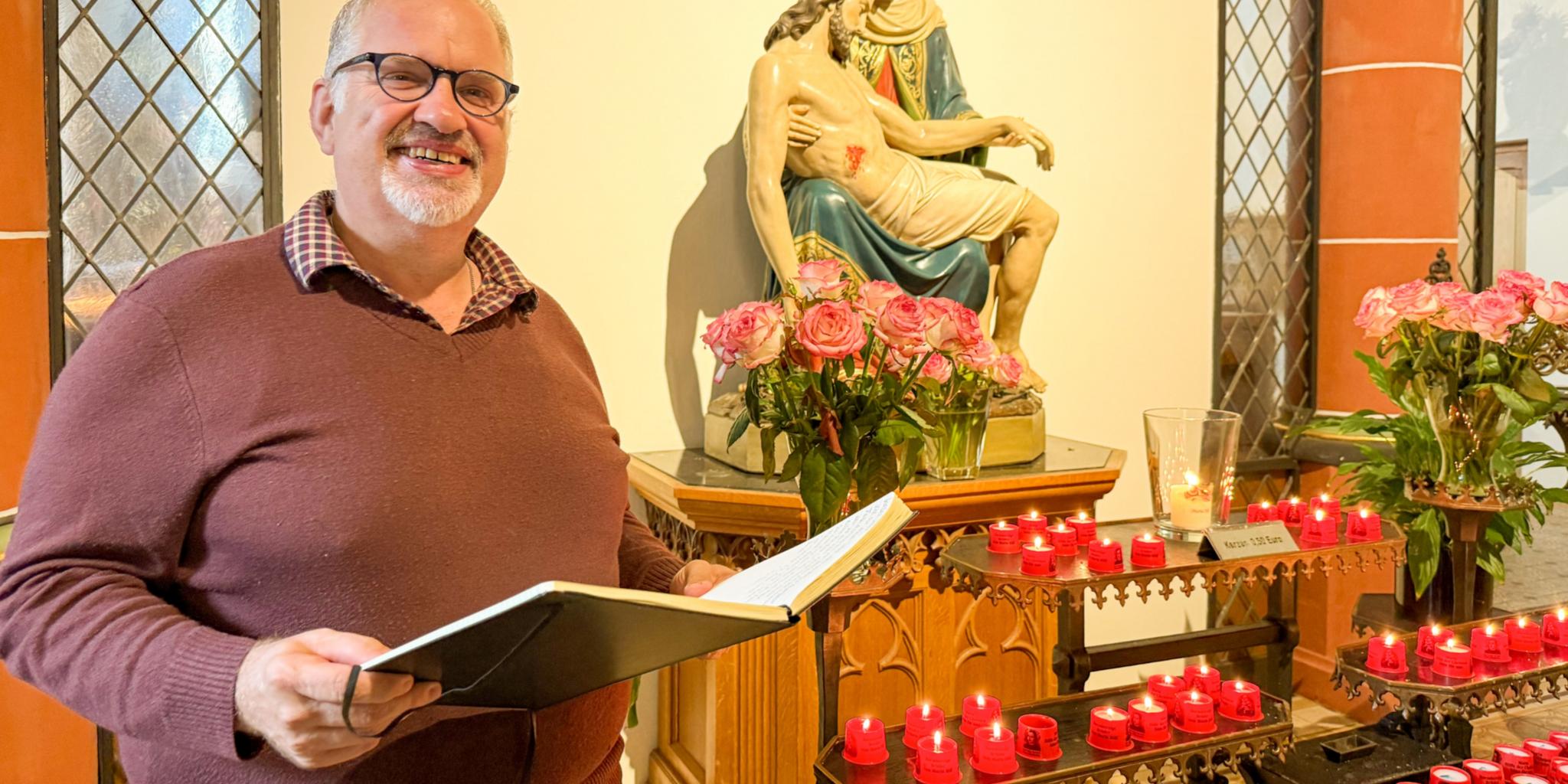 Bruder Jörg mit einem aufgeschlgenen Buch vor der Pietà in der Klosterkirche des Trierer Brüderkrankenhauses.