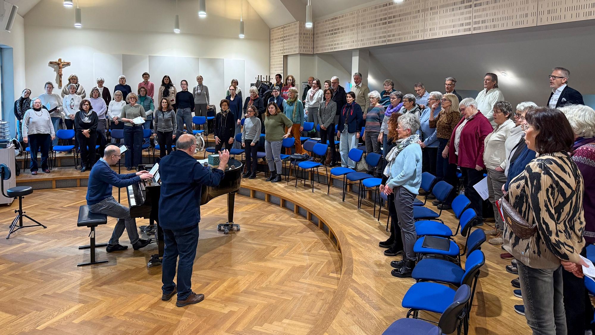 Ein Chor steht im Halbkreis um Dirigent und Pianist.