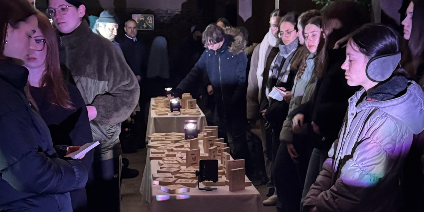 Teilnehmer der Gedenkveranstaltung stehn um Tische mit Holzplättchen zum Gedenken an die einzelnen Deportierten.