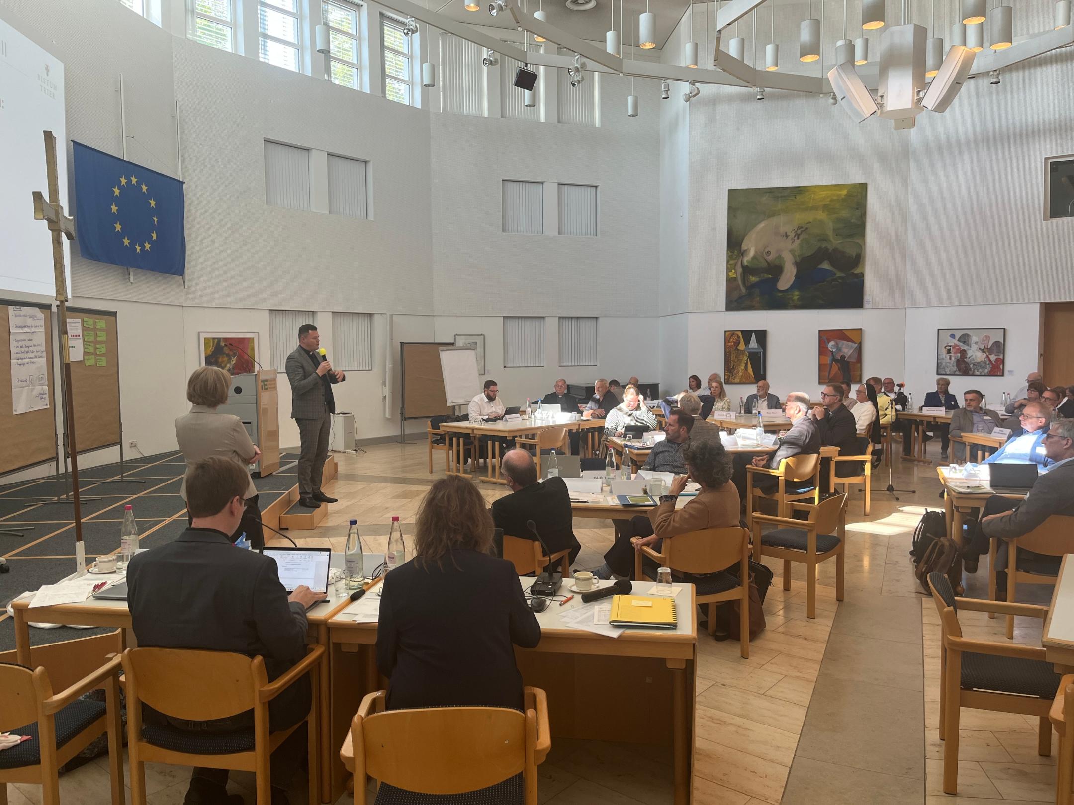 Blick in den Sitzungsraum, in dem viele Personen vor ihren Laptops sitzen.