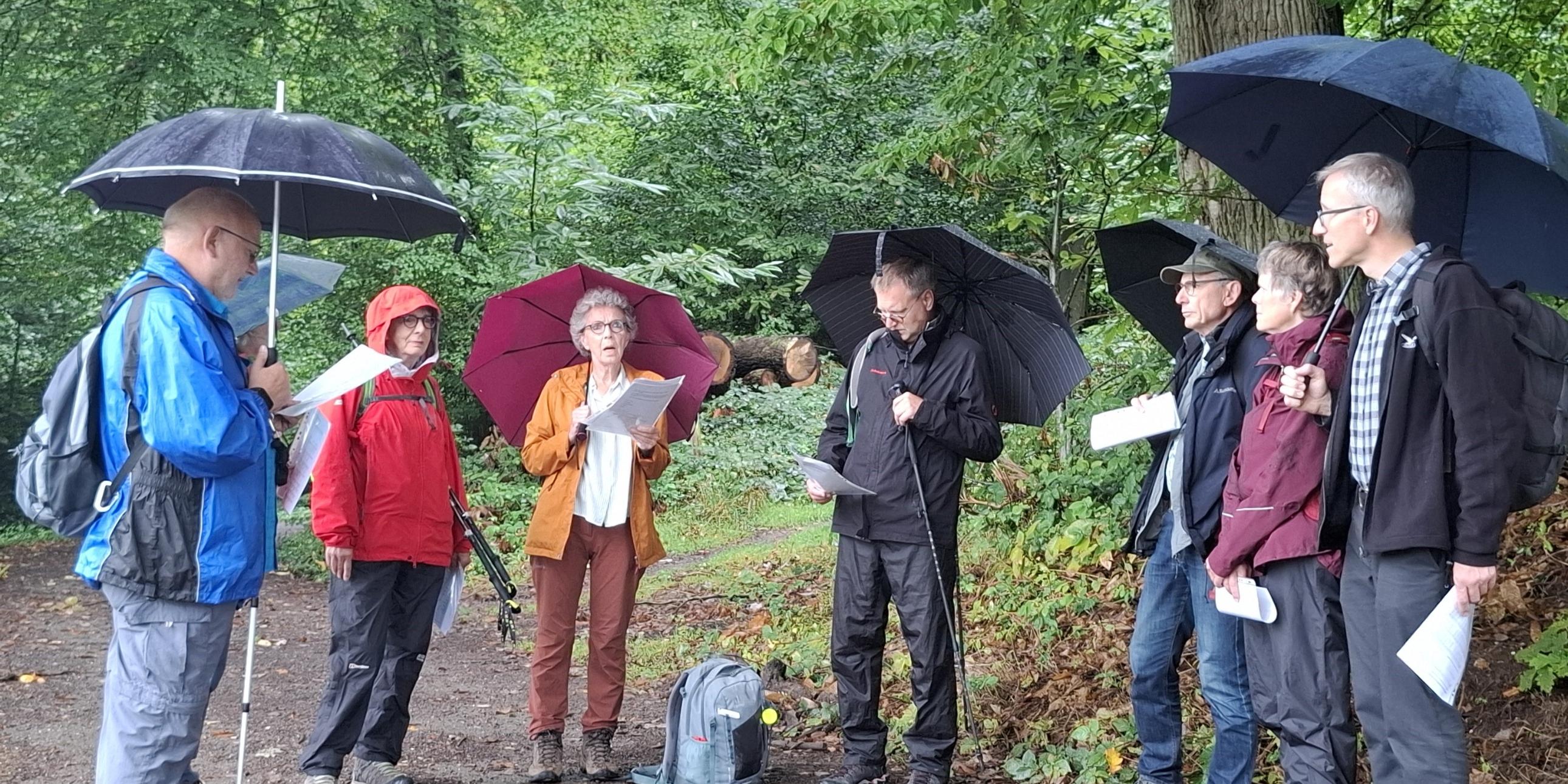 Gruppe mit Regenschirmen und Textblättern beim gemeinsamen Impuls.
