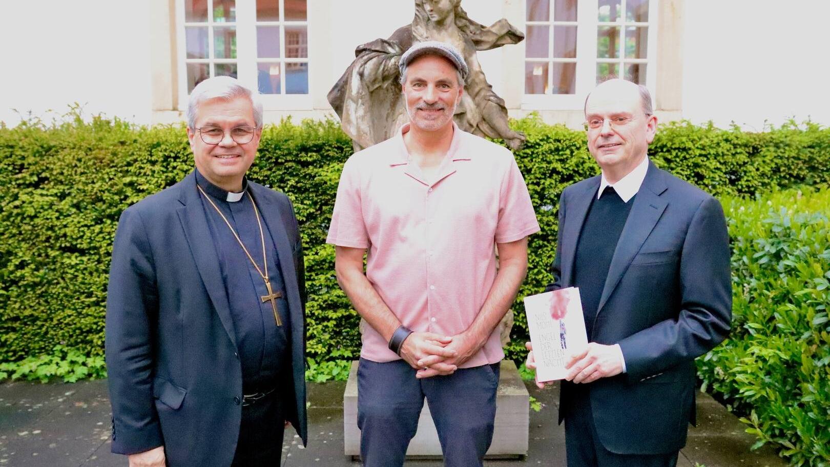 Drei Männer stehen vor einer Skulptur und lächeln in die Kamera
