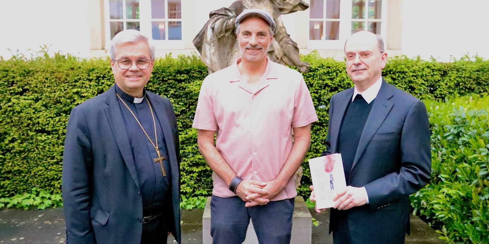 Drei Männer stehen vor einer Skulptur und lächeln in die Kamera