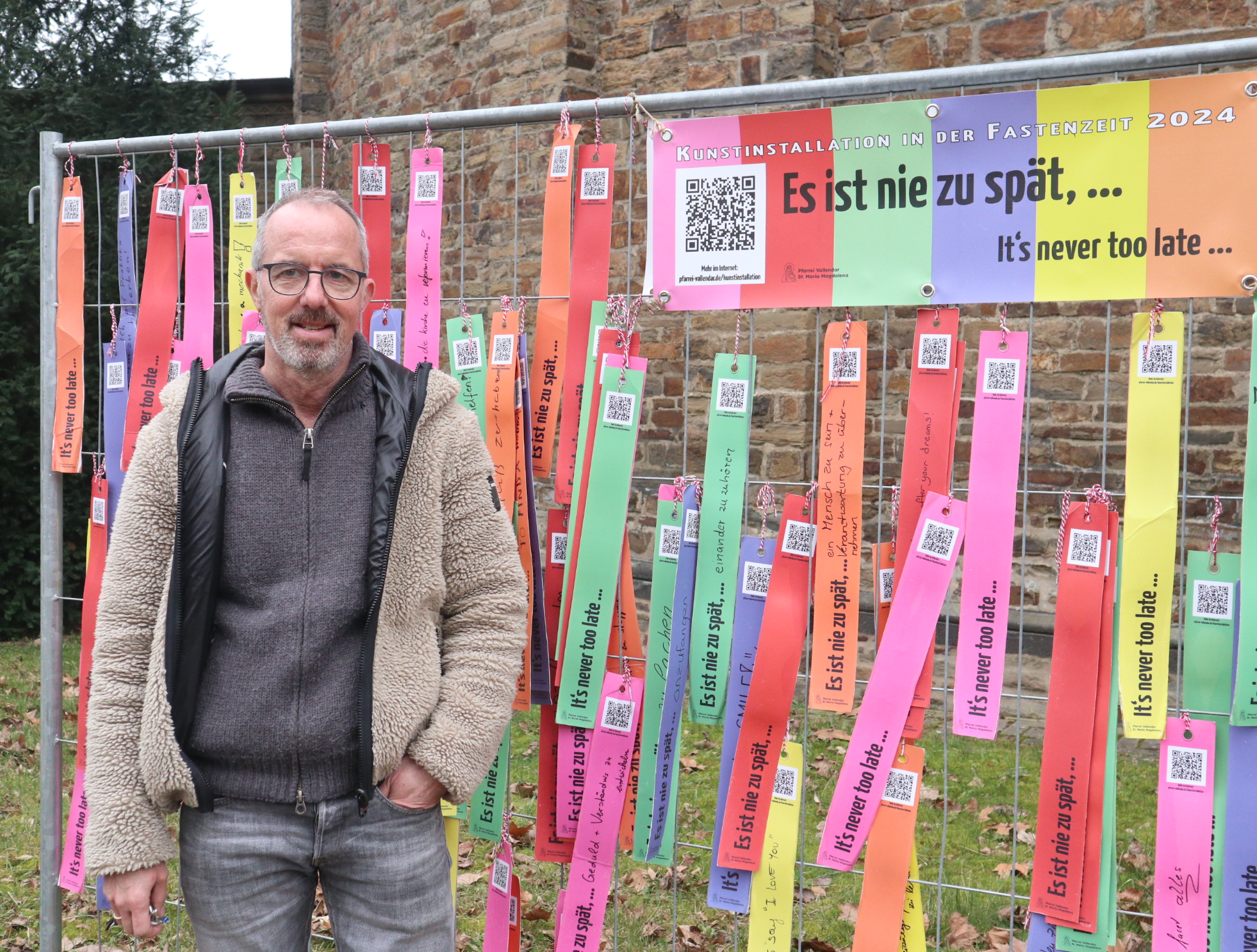 Mann vor Bauzaun mit vielen bunten Zetteln.