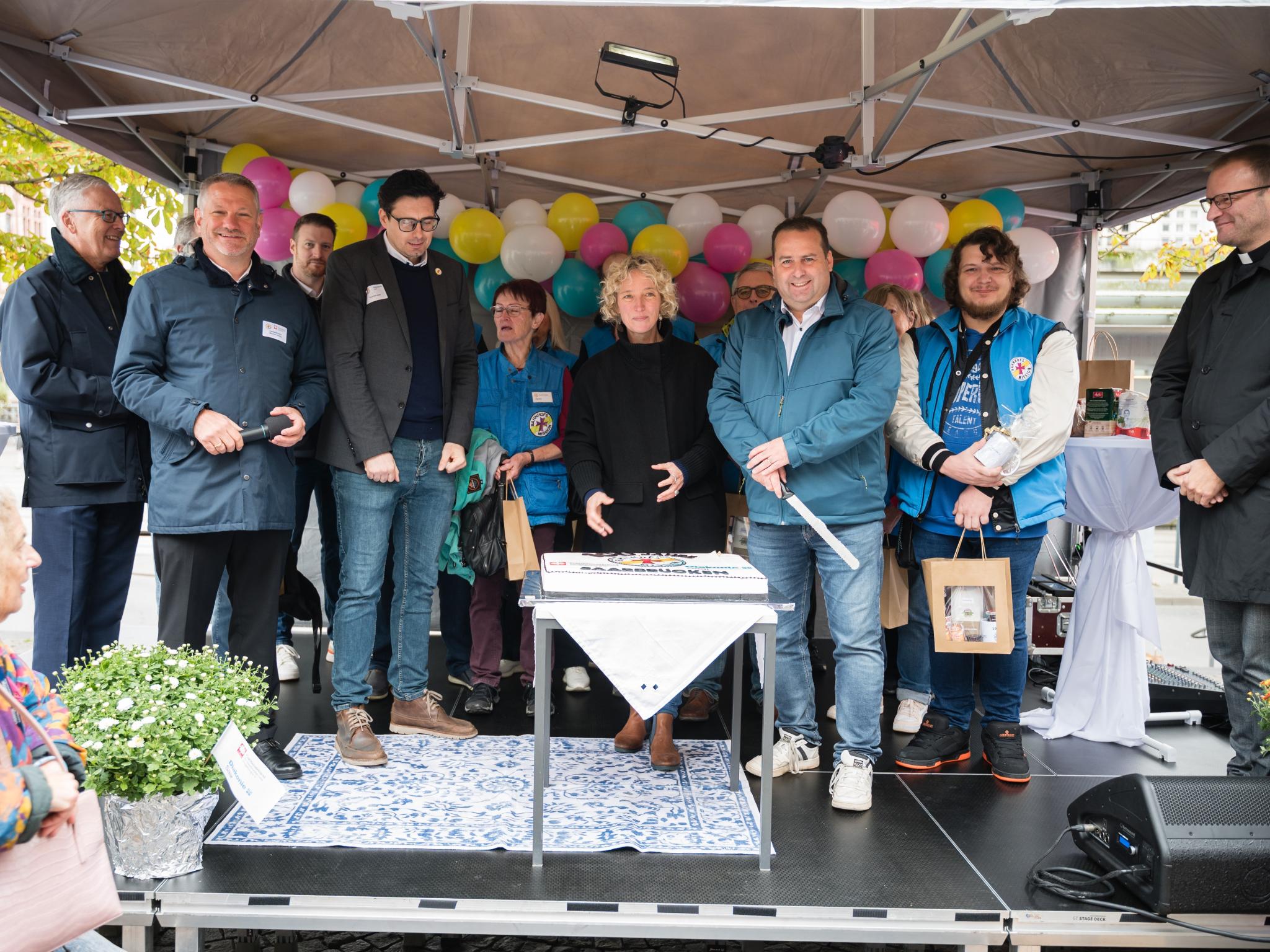 Sozialminister Dr. Magnus Jung (3.v.r.) schnitt mit Jennifer Sauer, Leiterin Bahnhofsmanagement (Mitte), und Tafelkoordinator Thorsten Junk (4.v.l.) die Torte an. Es feierten mit (v.l.n.r.): Dr. Klaus Vornhusen (Deutsche Bahn), Caritasdirektor Michael Schley und Tobias Raab sowie viele Ehrenamtliche.