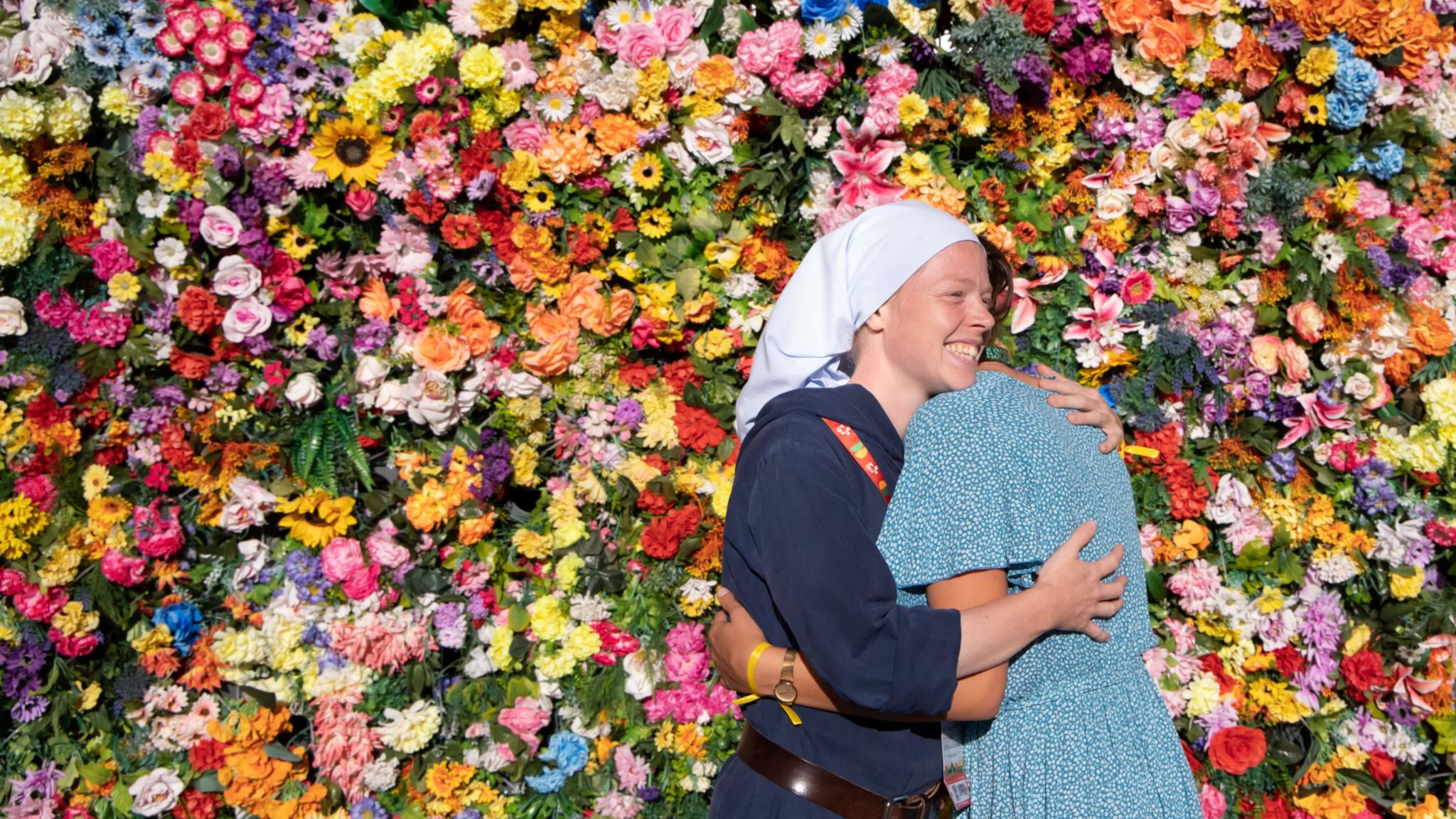 Zwei Frauen umarmen sich vor einer Wand aus Blumen.