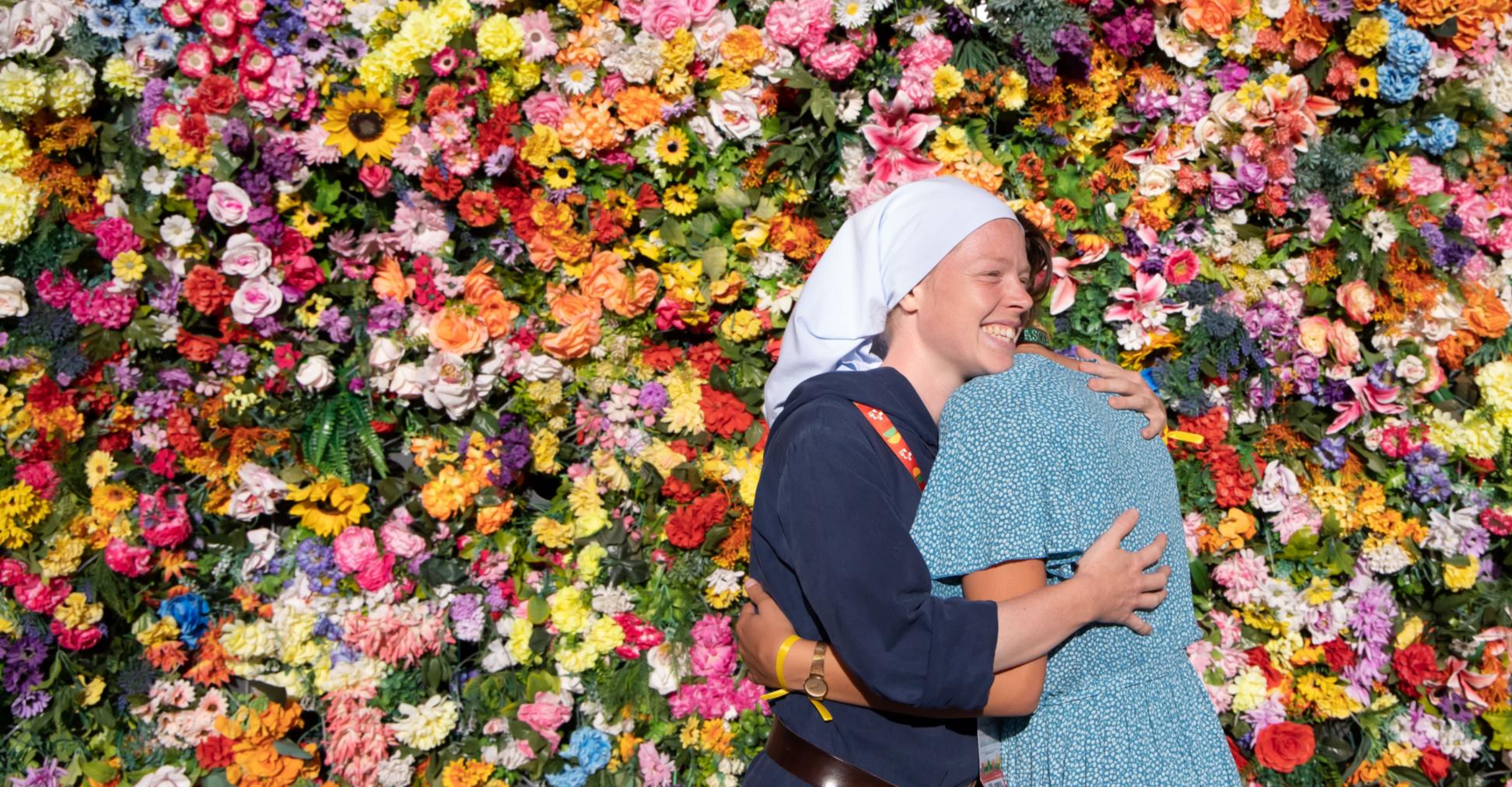 Zwei Frauen umarmen sich vor einer Wand aus Blumen.