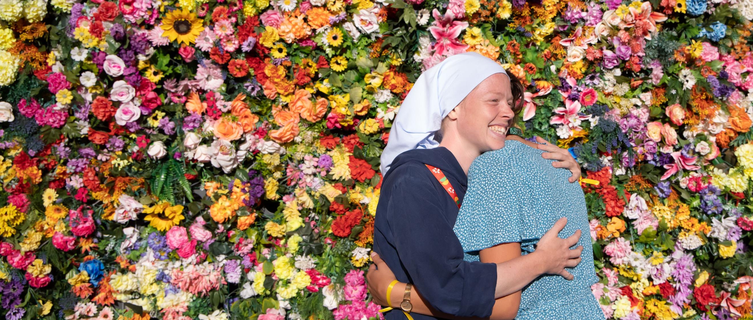 Zwei Frauen umarmen sich vor einer Wand aus Blumen.