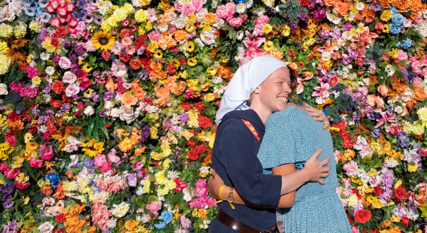 Zwei Frauen umarmen sich vor einer Wand aus Blumen.