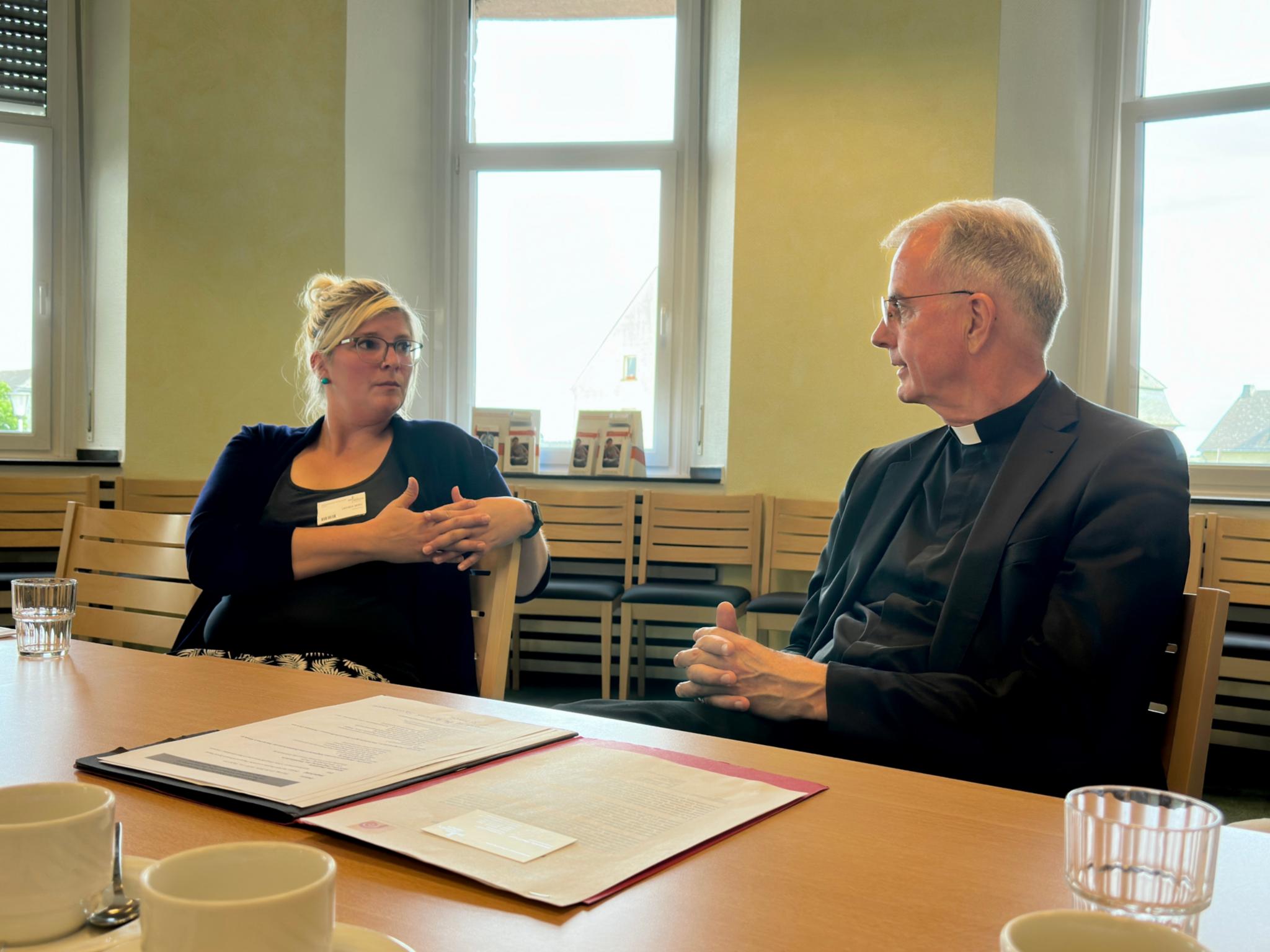 Links im Bild sitzt die Hebamme Desiree Berg. Sie ist im Gespräch mit Weihbischof Peters, der rechts neben ihr an einem Tisch sitzt, über die Unterstützung von Sternenkinder-Familien