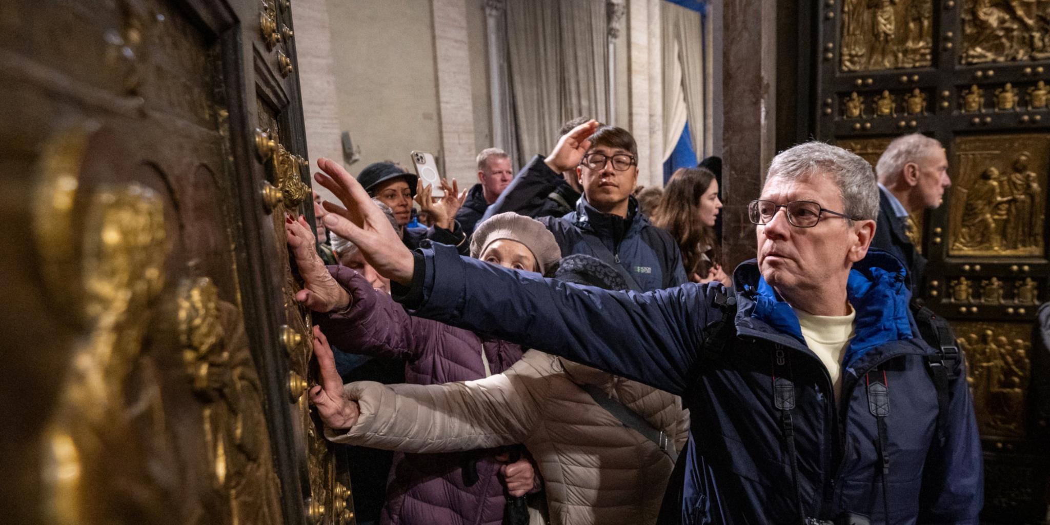 Pilger berühren  beim Durchschreiten die Heilige Pforte im Petersdom im Vatikan.