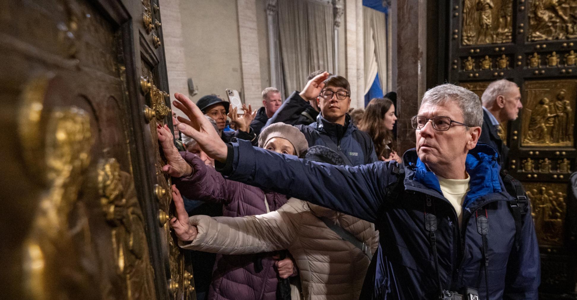Pilger berühren  beim Durchschreiten die Heilige Pforte im Petersdom im Vatikan.